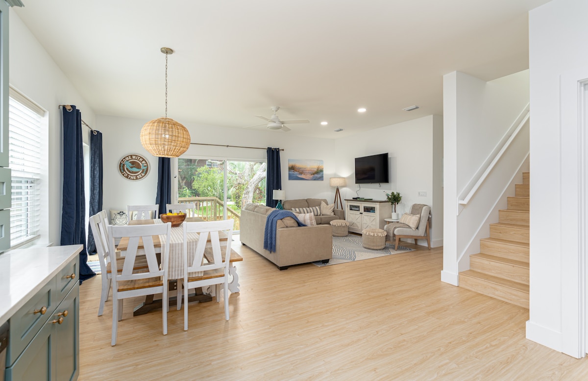 One open room holds all of it - the long farmhouse table, the sofas, and the stairs up to the second suite. Nine people can be doing nine different things down here and still feel like they are spending the day together.