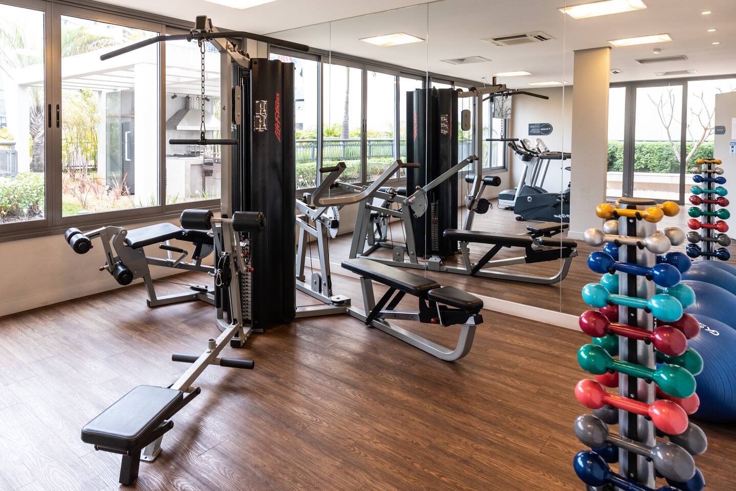 Espaço de musculação com pesos livres, estação multiuso e vista iluminada.
