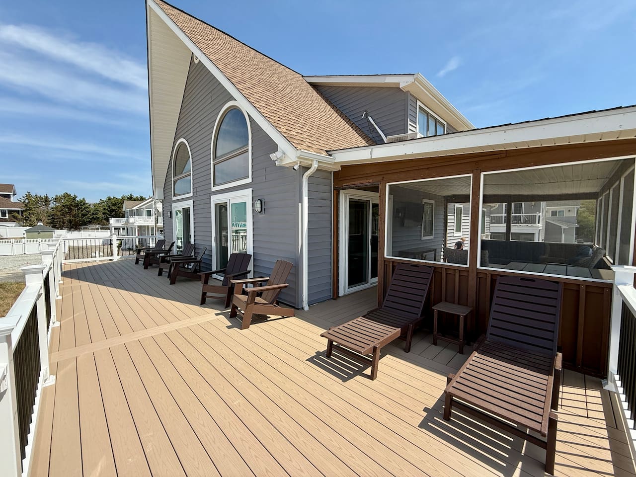 You can see an expansive outdoor deck featuring comfortable seating arrangements, including multiple lounge chairs and Adirondack-style chairs. This inviting space serves as an excellent spot for relaxing outside adjacent to the home.