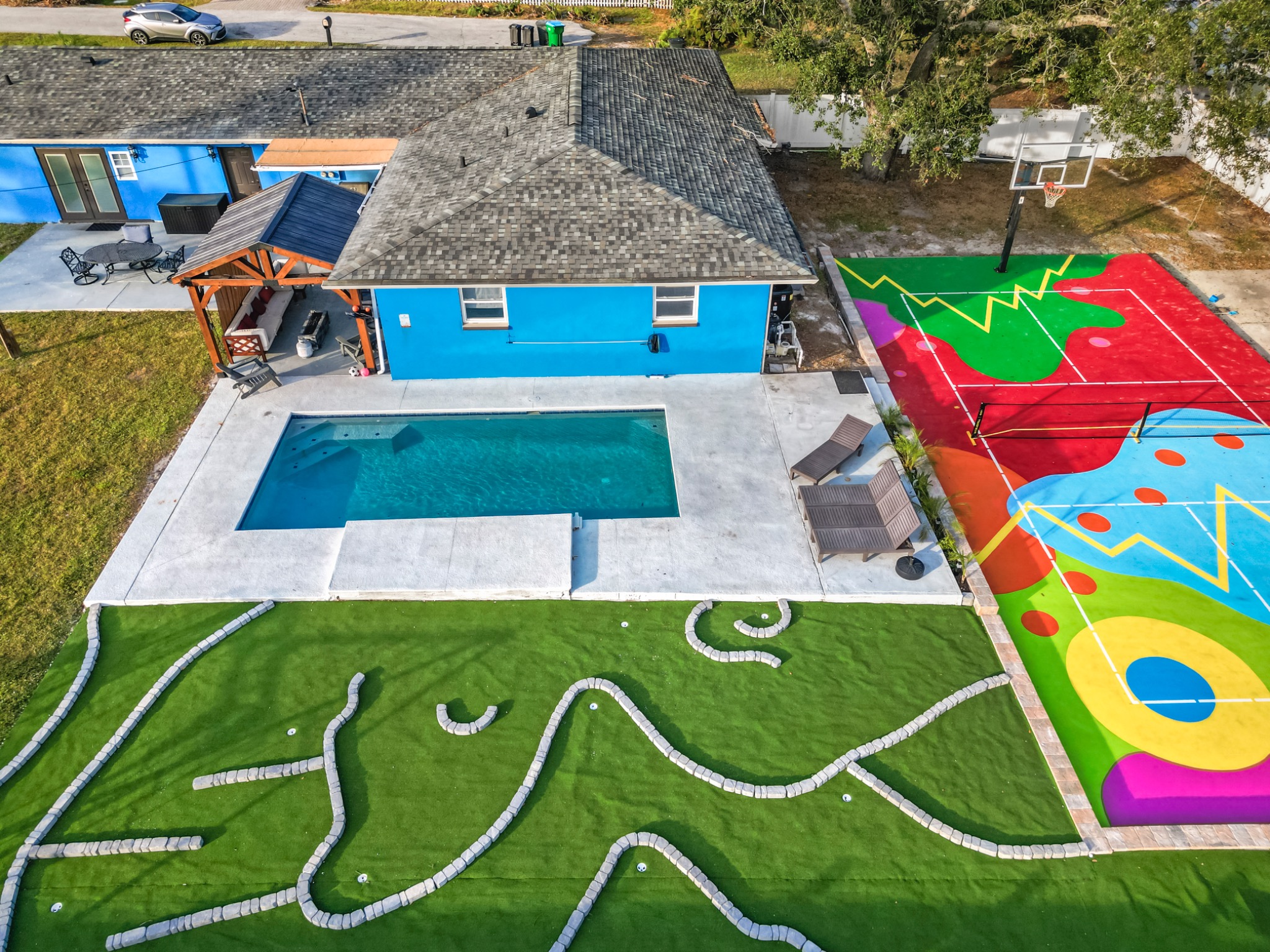 Beautiful exterior view of backyard with put put, pool, and pickleball/basketball