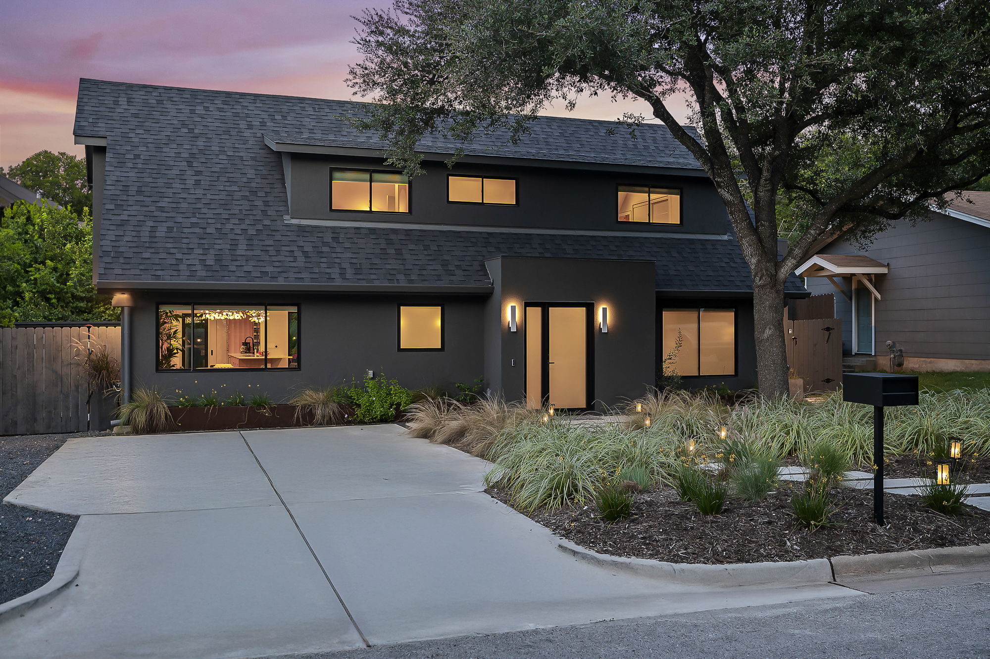 A stunning modern home with a dark gray facade and a prominent A-frame roof is captured at dusk, with its well-lit exterior and minimalist landscaping.