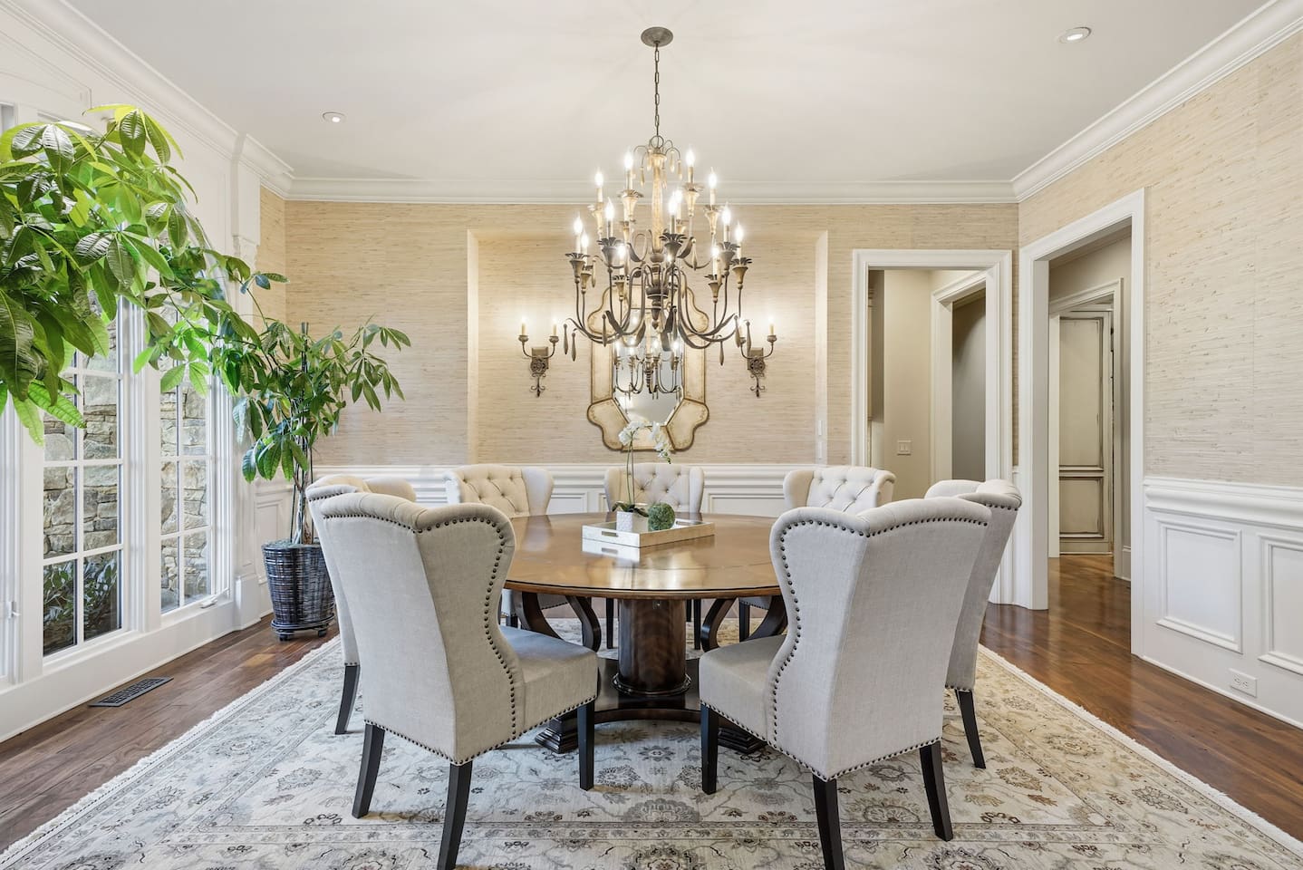 Spacious main dining room to the left of the foyer, featuring a chandelier, seating for seven, and lush green plants. A bright, welcoming space perfect for shared meals or special gatherings.