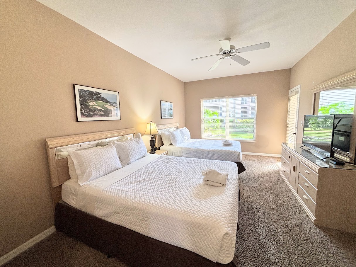 Comfortable bedroom featuring two beds, ceiling fan, TV, dresser storage, and plenty of natural light.