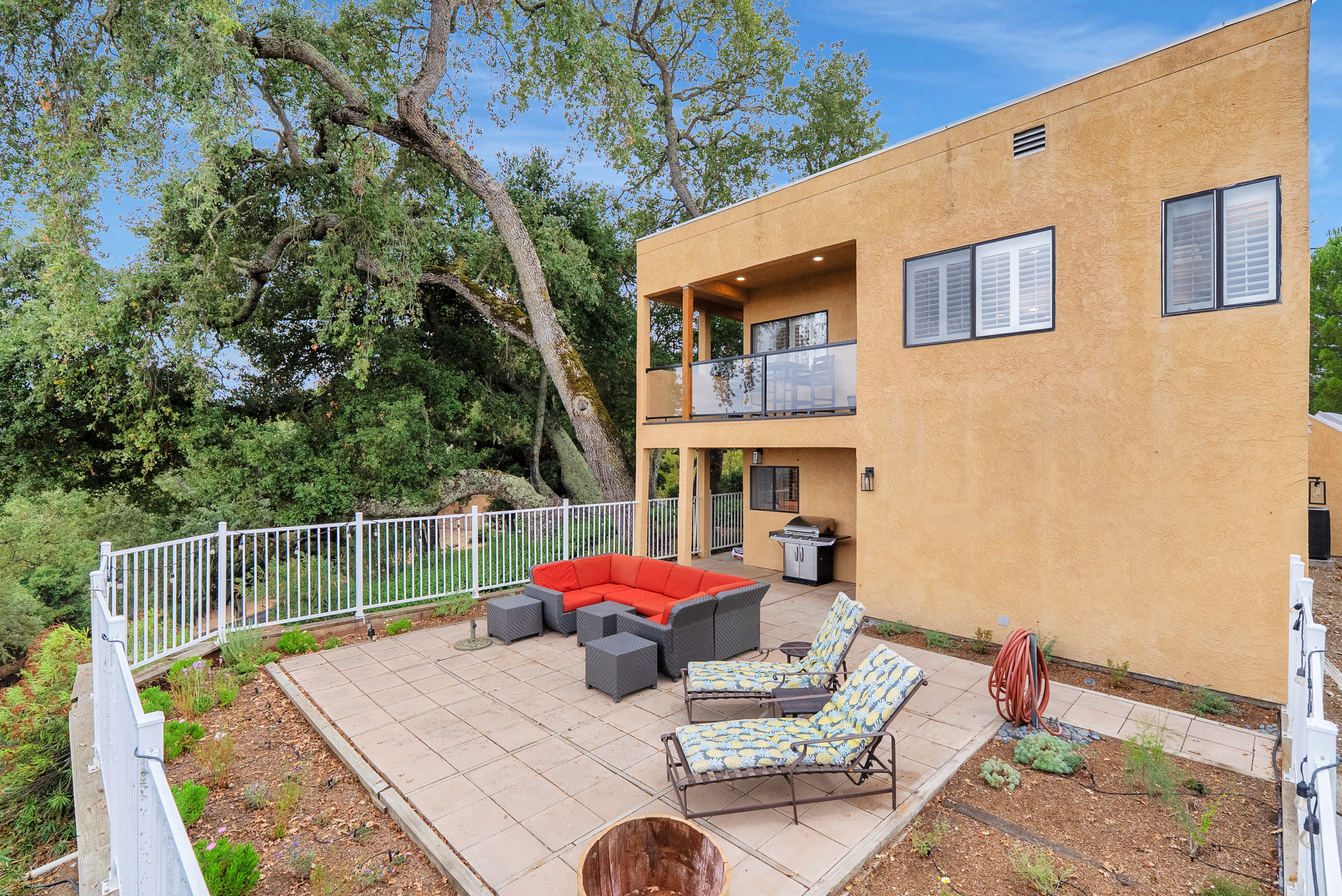 Enjoy the perfect blend of modern architecture and natural beauty. This home shows a lower patio for lounging on the vibrant sectional and grilling, complemented by an upper balcony for elevated views.