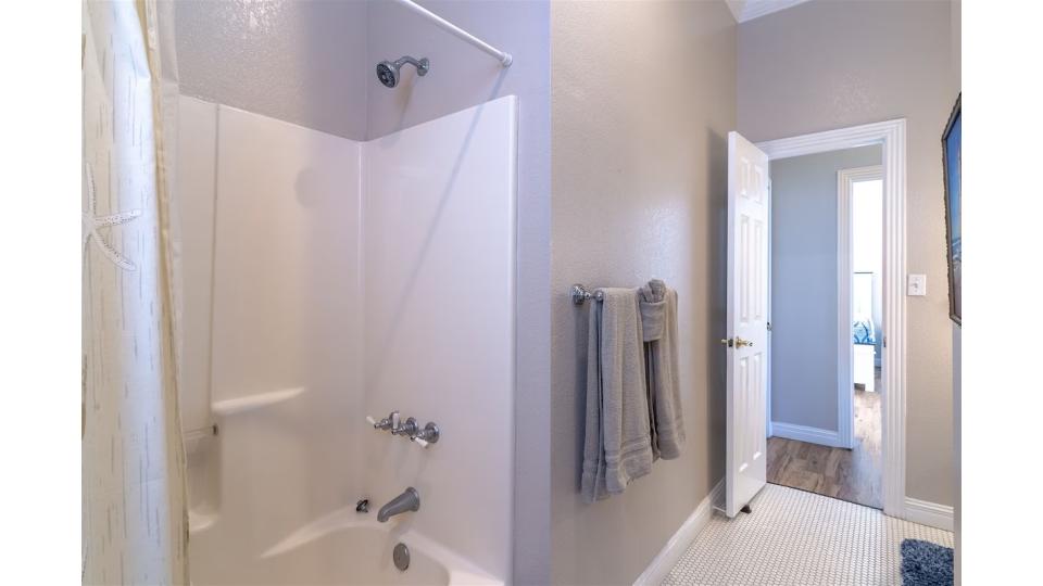 Sparkling clean bathroom with tub/shower combo, beadboard accents, and coastal-inspired decor. This well-appointed shared bathroom serves the bunk room and common areas with style and function