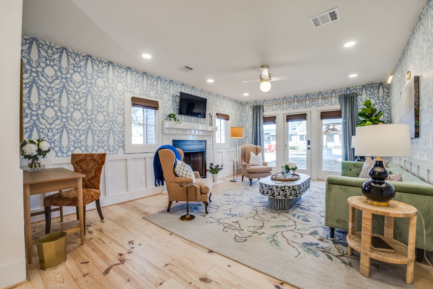 Bright and welcoming living room featuring designer wallpaper, cozy seating, and French doors that open to the spacious outdoor grounds.