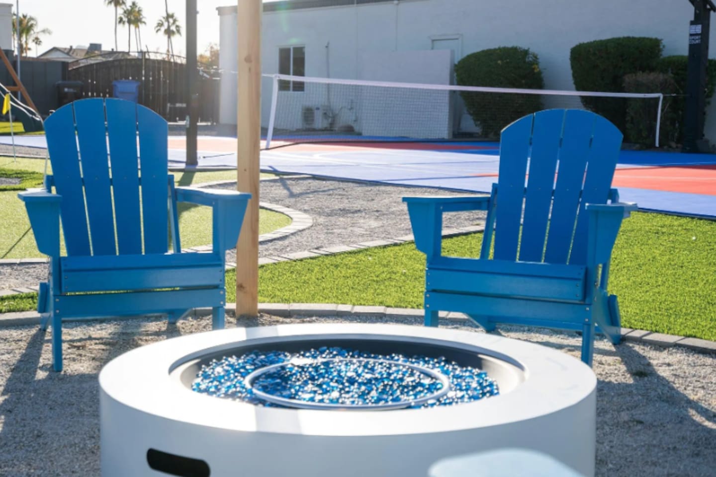 Blue Adirondack chairs circle the fire pit, with the sport court just steps away for guests who want to keep moving after dark.
