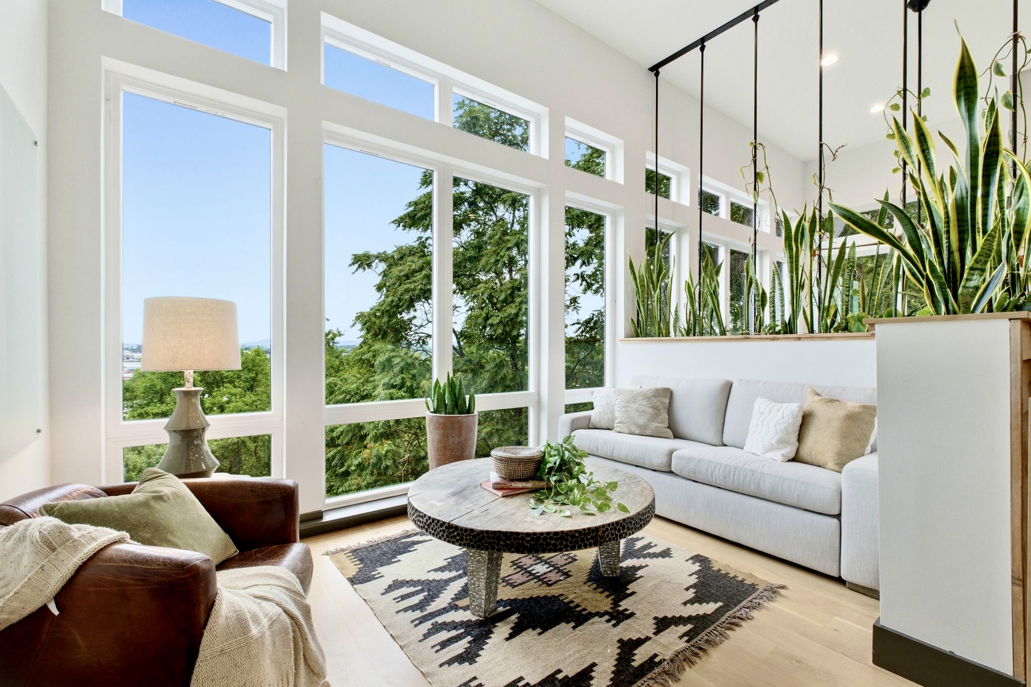 Light-soaked living area w/ floor-to-ceiling windows, white sofas & lush greenery all around.
