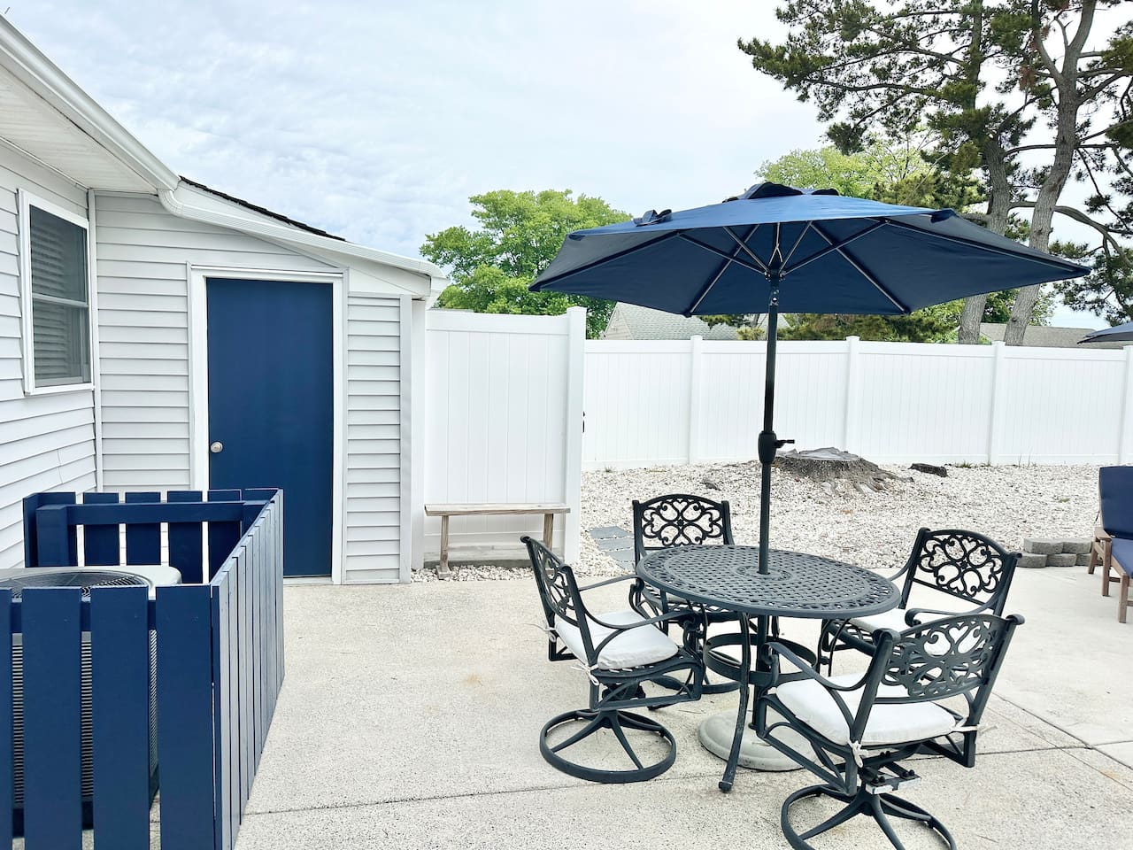 Enjoy meals at our outdoor dining set, featuring a stylish black metal table and four cushioned swivel chairs. A large navy umbrella provides plenty of shade on the spacious concrete patio, all within the privacy of a fully fenced backyard.