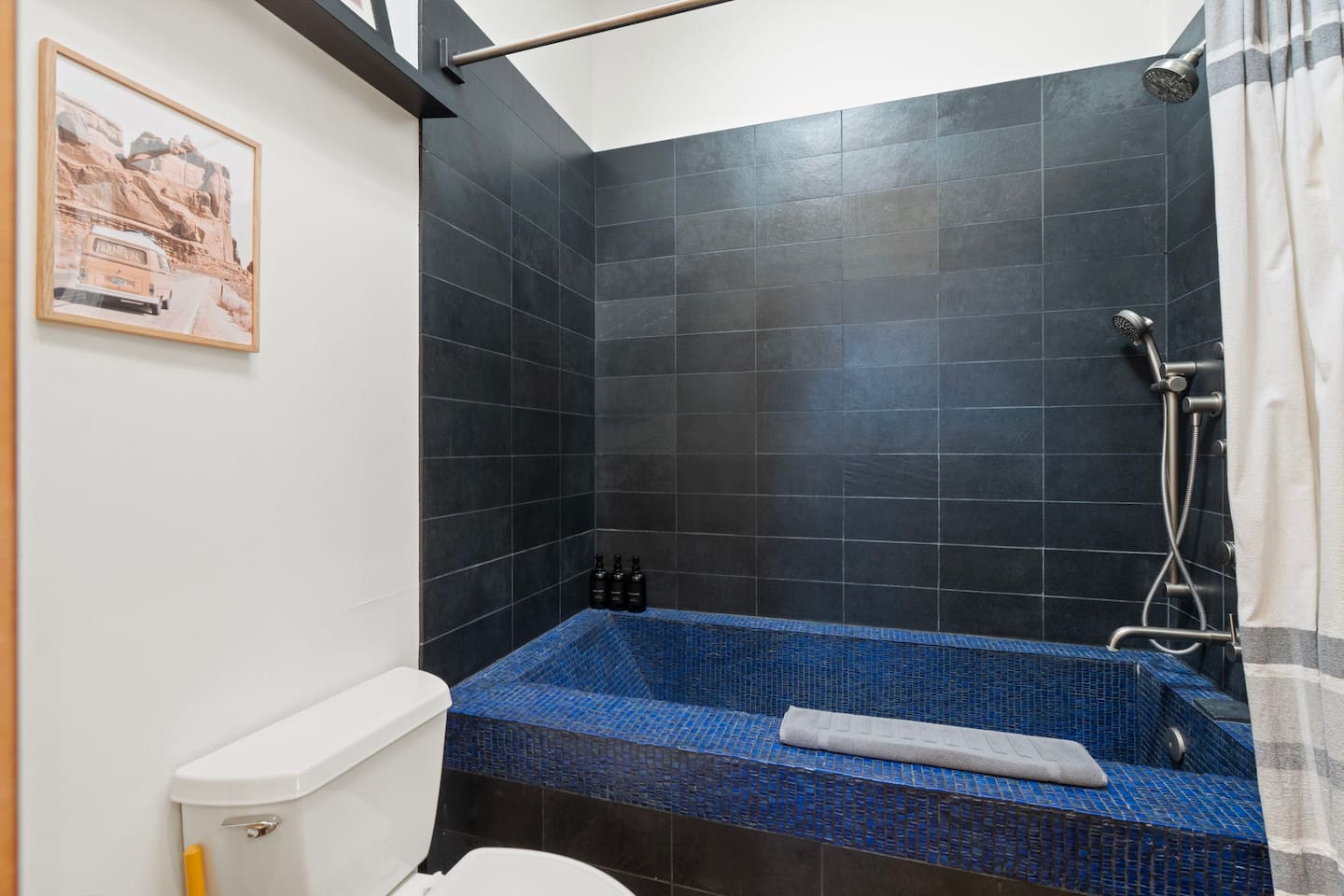 Modern bathroom with a deep blue tiled soaking tub, sleek black tile walls, and a rainfall shower for a spa-like feel.