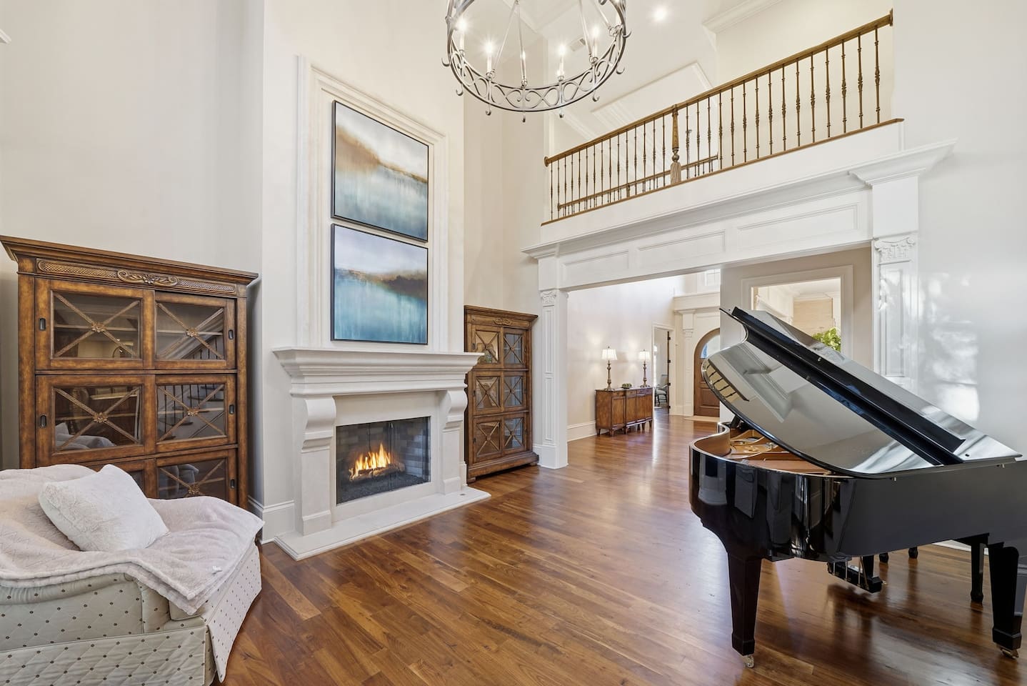 Beautiful entry sitting room with a grand piano, warm fireplace, tall windows, and two comfortable chairs. A bright, serene spot to unwind or enjoy quiet moments.