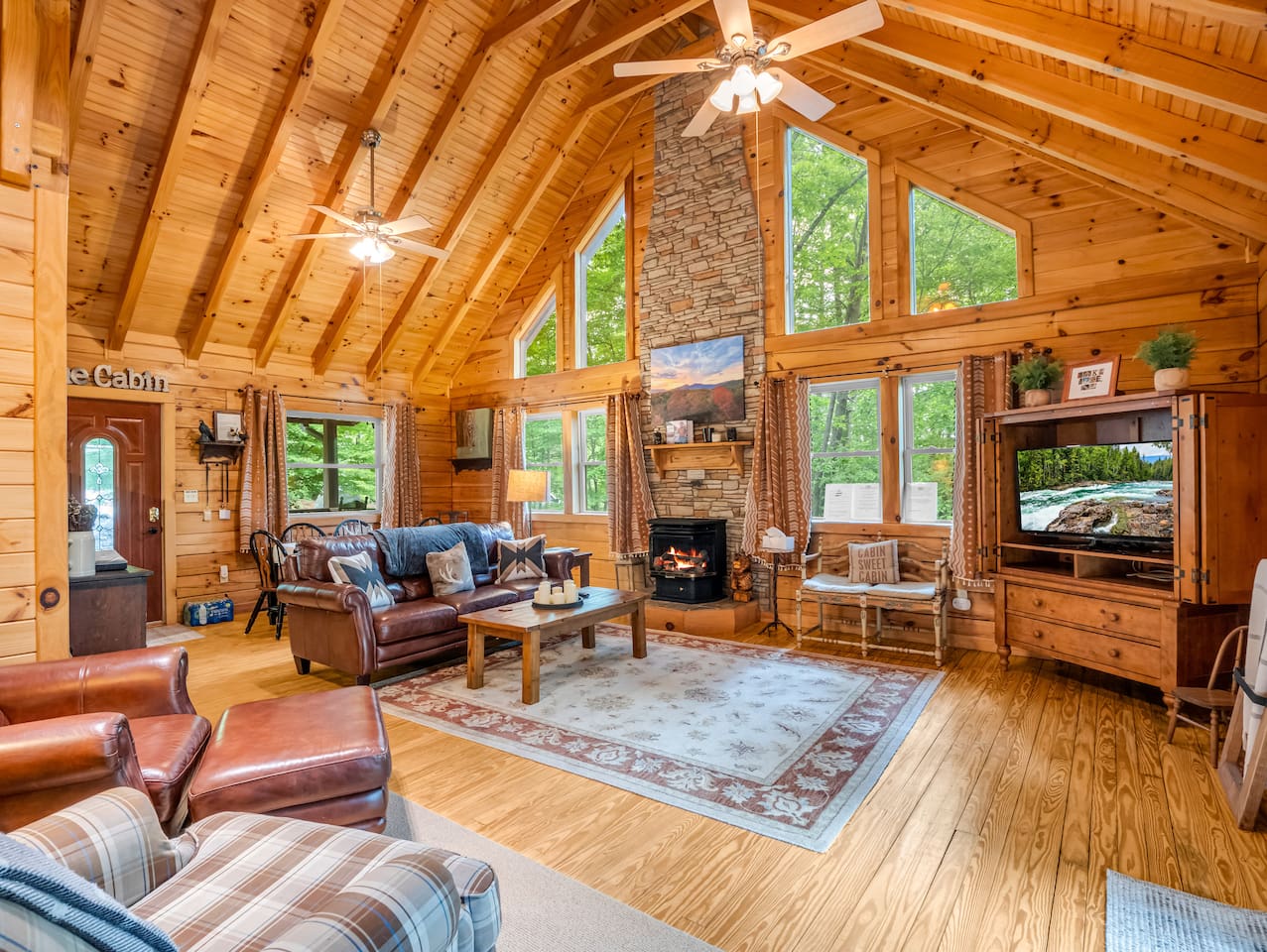 Main living room featuring high vaulted ceilings, stone fireplace and mantel, leather seating, and a television set