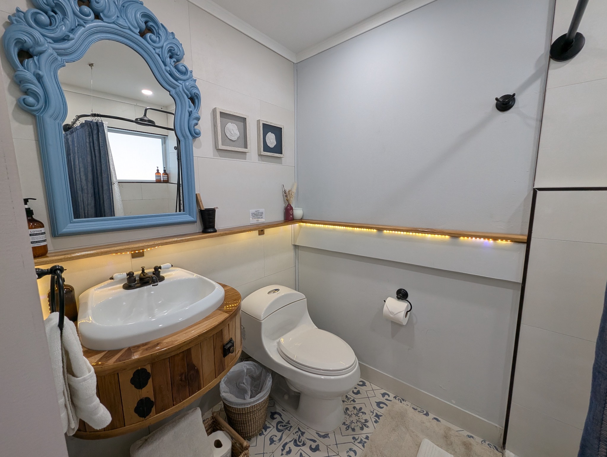Ensuite bathroom for the queen bedroom at Villa Coral featuring a custom wooden vanity, patterned blue floor tile, an ornate blue mirror, and warm LED accent lighting in Dorado, Puerto Rico.
