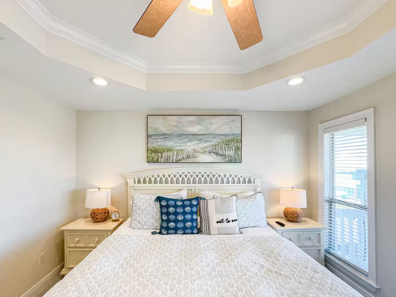 Serene bedroom with a comfortable queen bed, soft coastal decor, and plenty of natural light. Features bedside lamps, ceiling fan, and a peaceful atmosphere for restful nights.