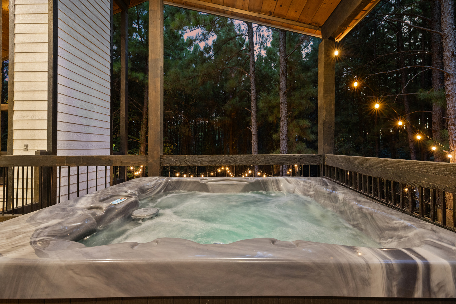 One last soak before bed. Slip into the hot tub beneath the covered deck while the string lights glow through the trees around you.