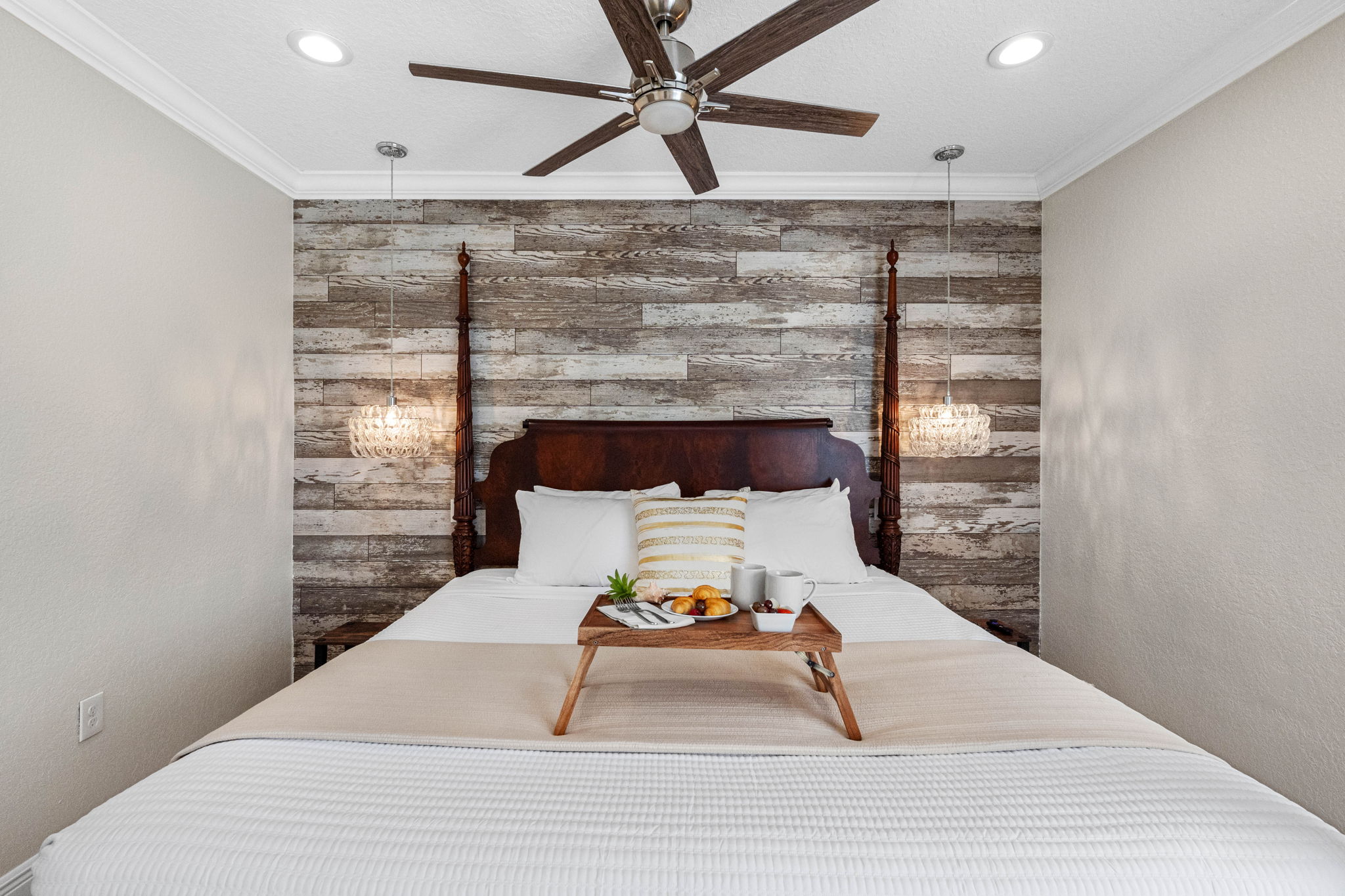 The wood-paneled accent wall and rich four-poster bed bring warmth and character, complemented by neutral tones and polished tile floors.