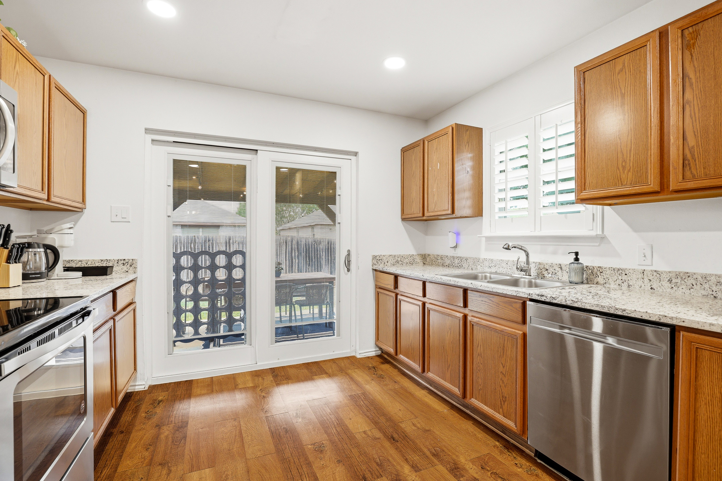 Full galley kitchen with electric stove, stainless dishwasher, granite countertops, ample cabinet space, and sliding glass door to the backyard. Everything stocked for home-cooked meals.