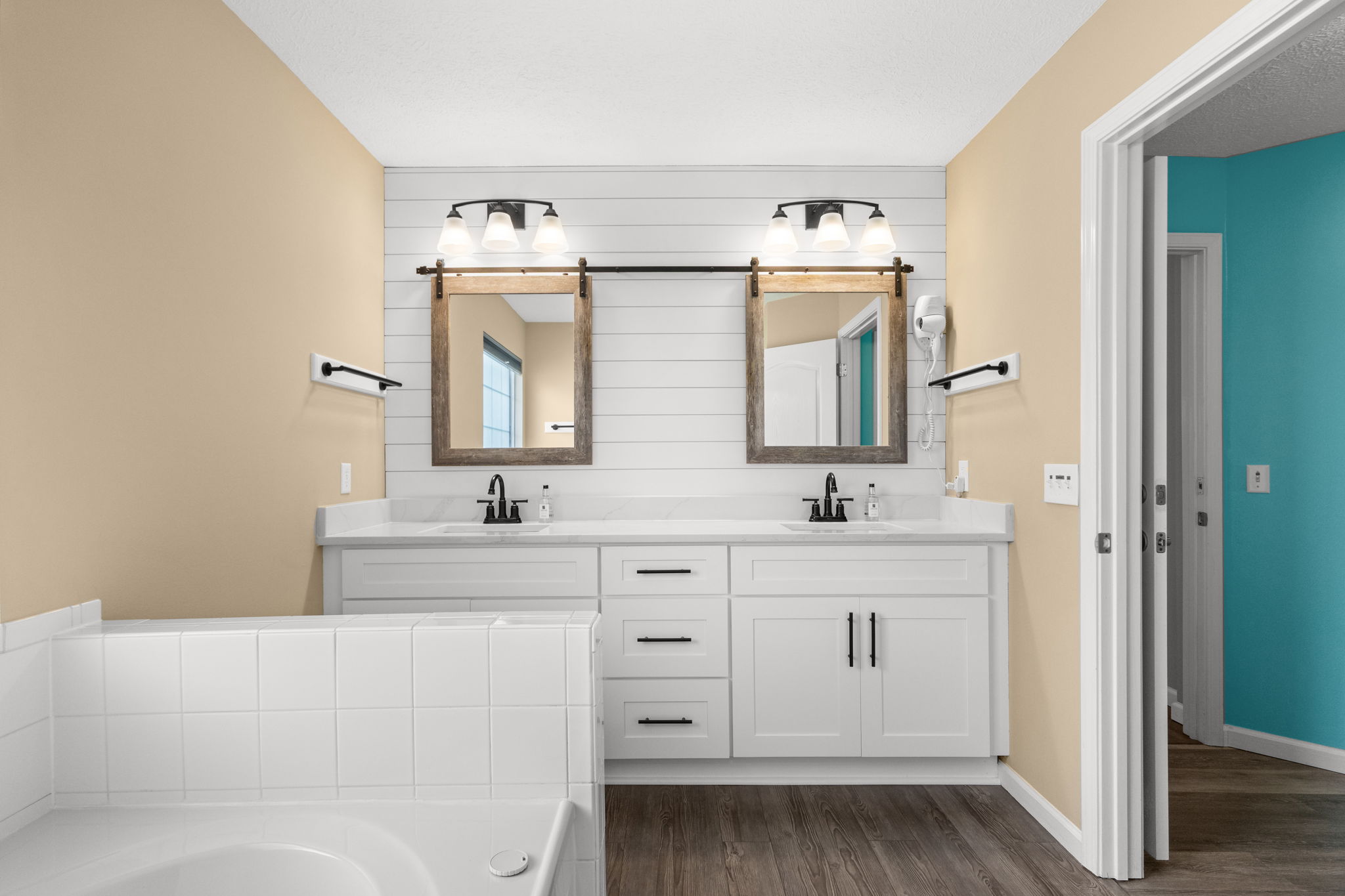 Spa-like master en-suite. This beautifully updated master bathroom features a spacious double vanity with ample storage, custom shiplap detailing, unique sliding barn-door mirrors, and a relaxing jacuzzi tub perfect for unwinding after a day at the beach.