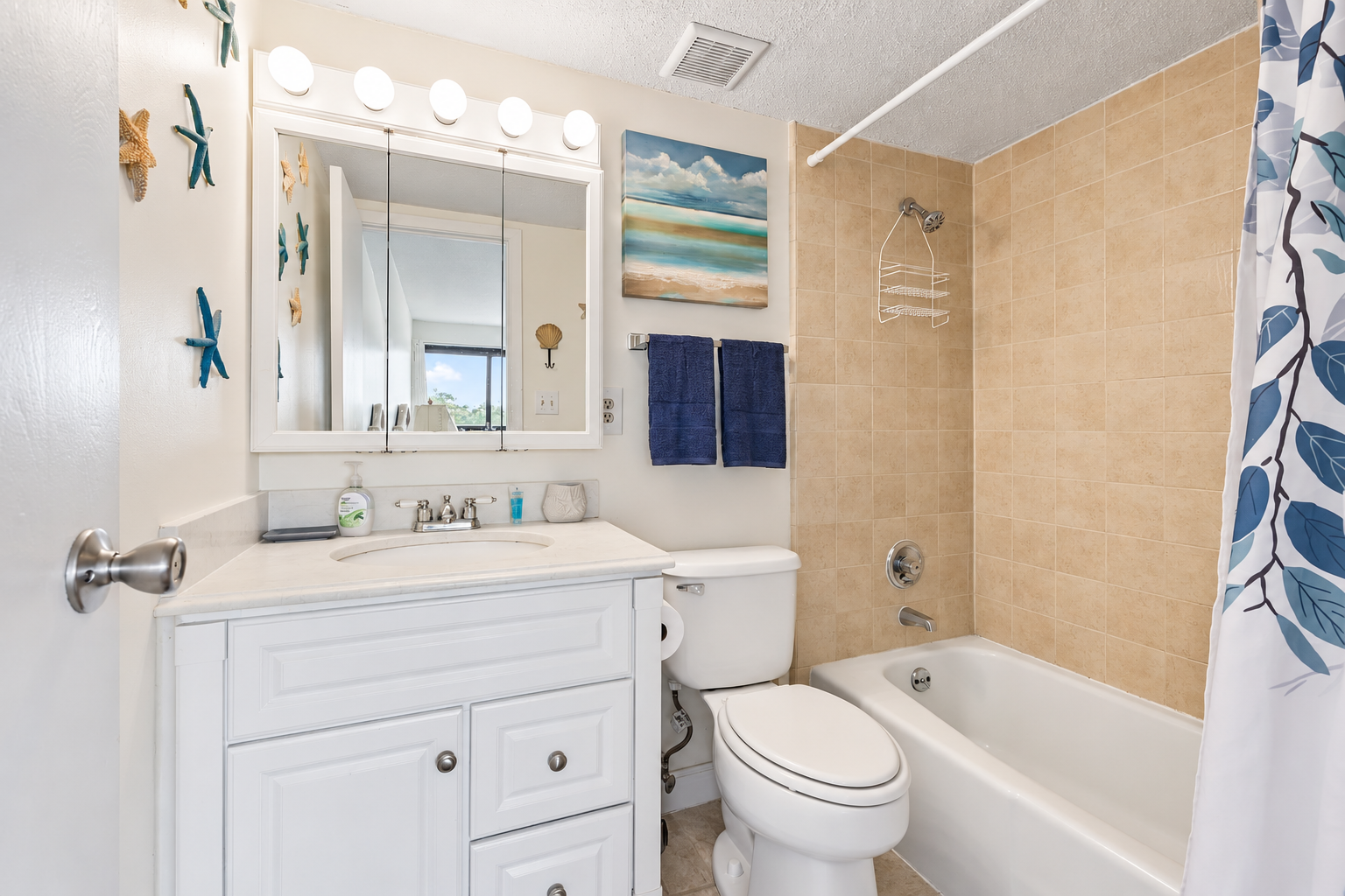 Ensuite bathroom with white vanity storage, shower/tub combo, and beach-themed wall details.