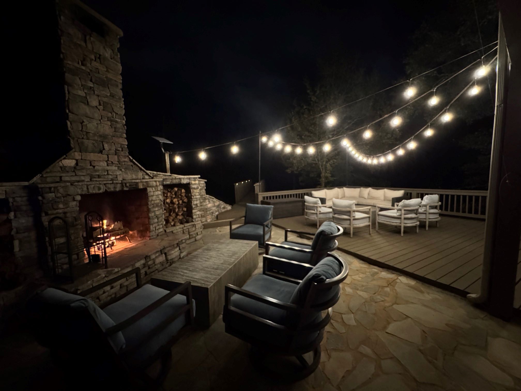 Enjoy party lights at night around the outdoor fireplace, creating a warm and inviting atmosphere for evening gatherings by the lake.
