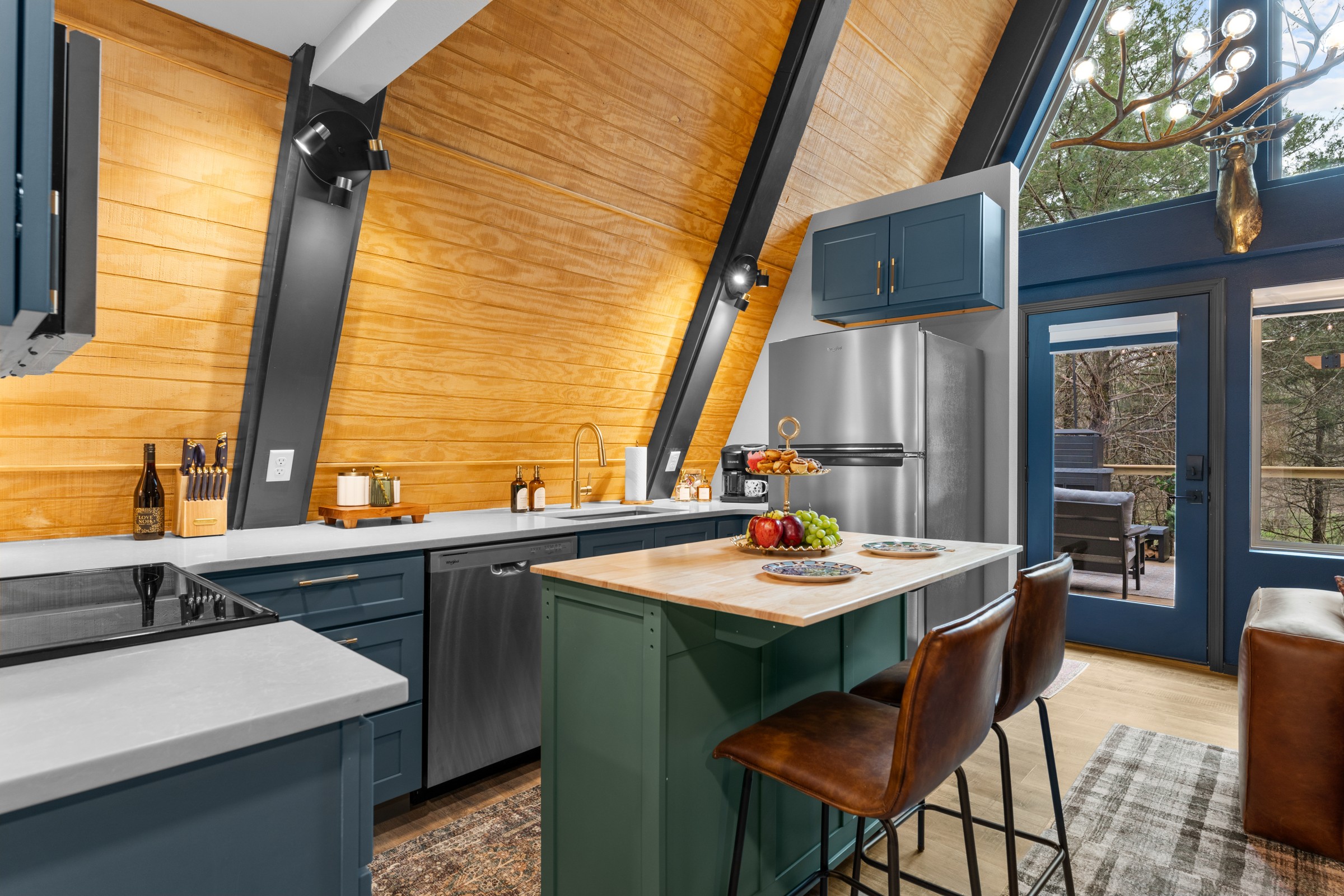 Kitchen with navy cabinets and a green island with two stools. Dishwasher, full-size fridge and a glass door out to the deck.