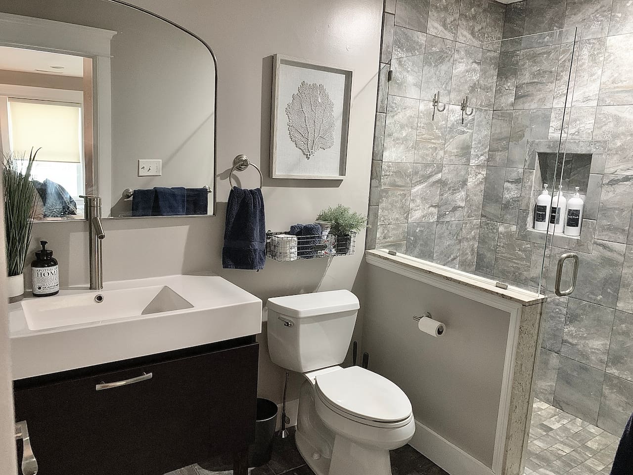 Refresh in this sleek bathroom featuring a modern vanity and a custom glass-enclosed shower with elegant grey tiling. Coastal artwork and a minimalist design create a spa-like atmosphere for your morning routine.