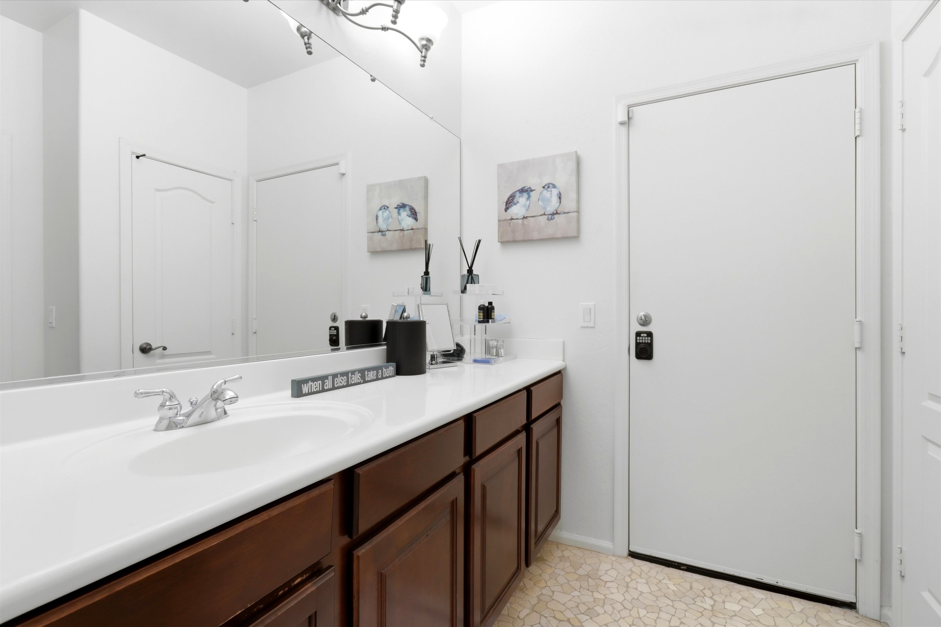 Bathroom vanity with a wide counter, storage cabinets, and guest essentials by the door.
