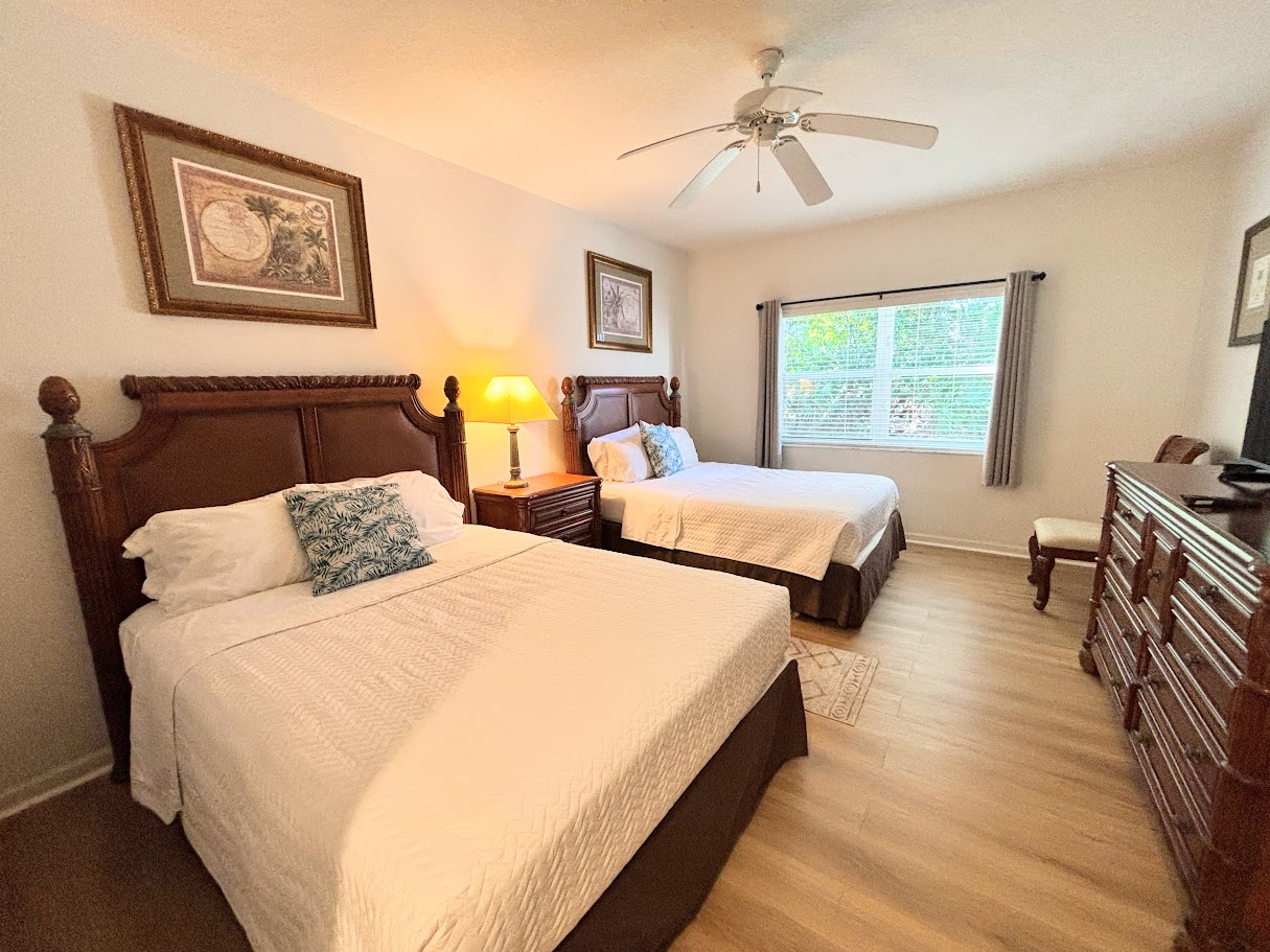 Comfortable bedroom featuring two beds, wood-look flooring, dresser storage, and plenty of natural light.