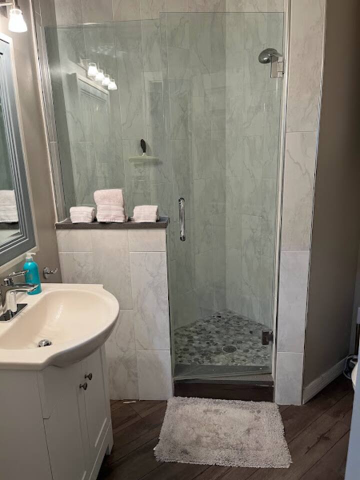 Updated bathroom featuring a walk-in shower, modern tilework, vanity space, and clean neutral finishes.
