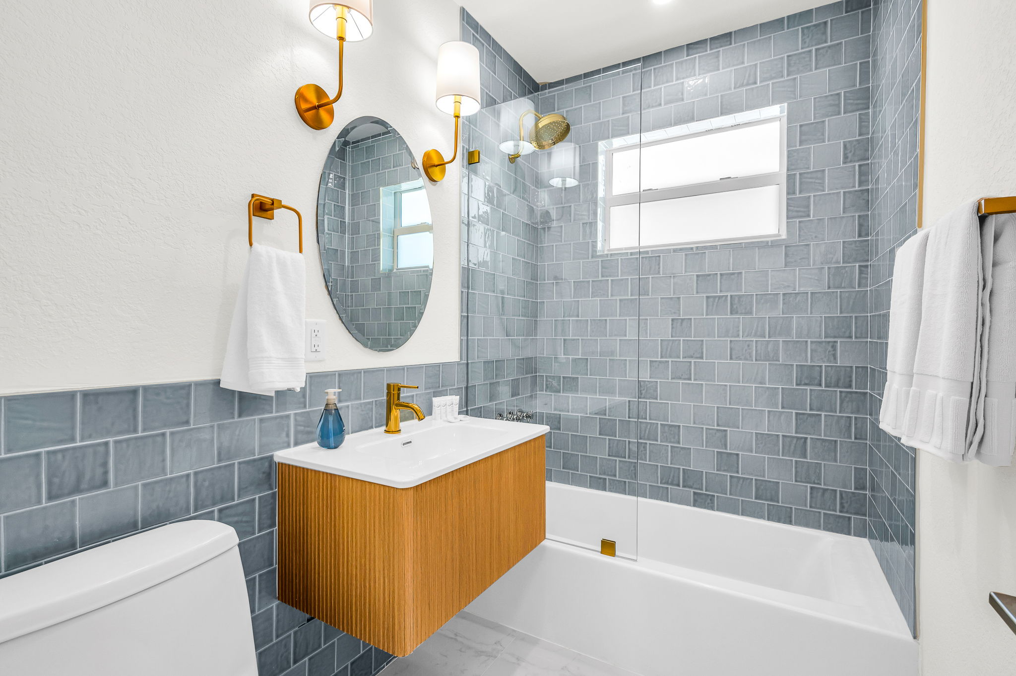 Fully renovated designer bath shared between bedrooms 2 and 3, featuring chic blue tile, gold fixtures, a modern vanity, and a sleek glass-enclosed shower-tub combo for a spa-inspired experience.