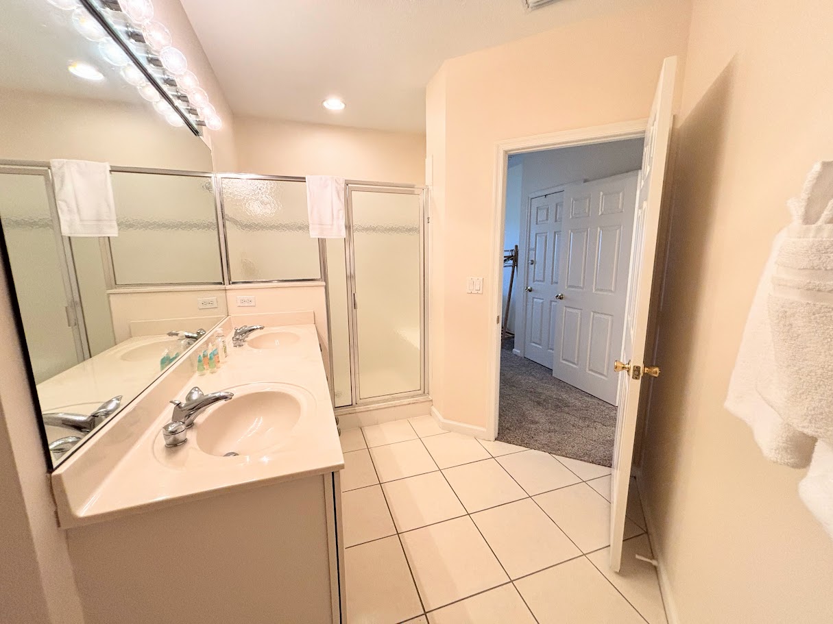 Bright bathroom with large vanity, full mirror, tile flooring, and a walk-in shower with glass doors.