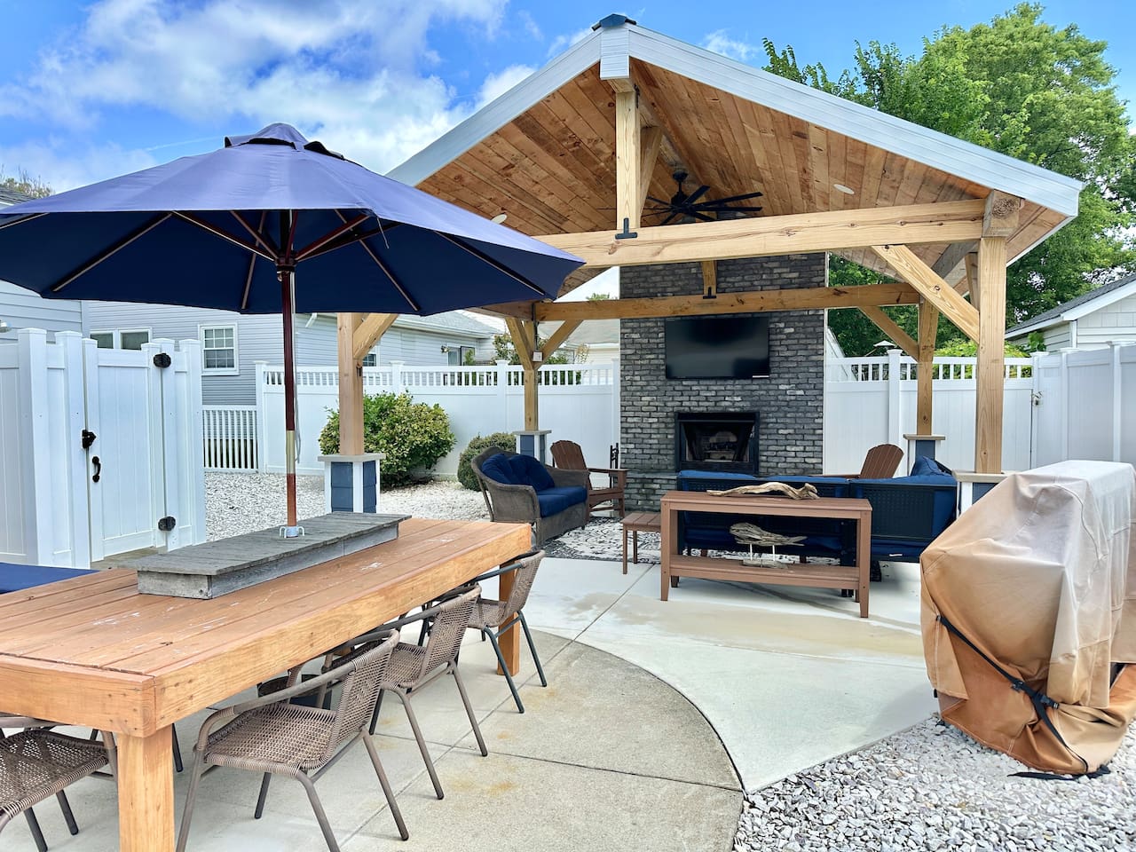 Savor alfresco meals at the spacious wooden dining table in your private backyard. This inviting space connects to a luxury covered lounge with a stone fireplace and TV, creating the ultimate setting for vacation entertaining.