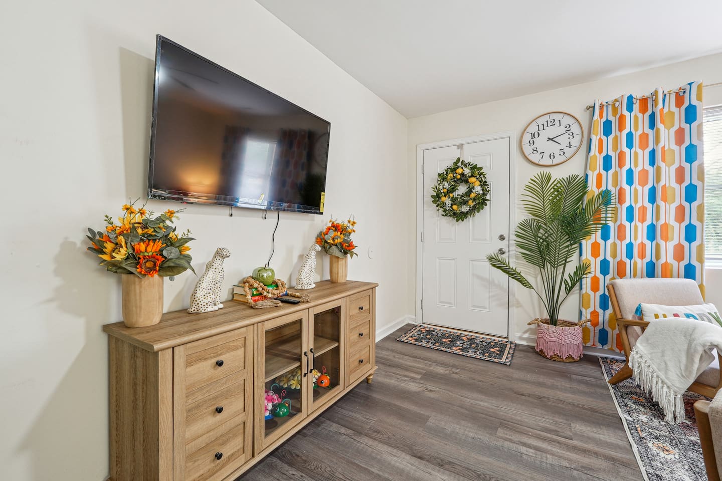 Enjoy a cozy living room featuring a long comfortable sofa, a TV for your entertainment, a ceiling fan, two chair, and a window with a lovely view outside — perfect for relaxing and unwinding.
