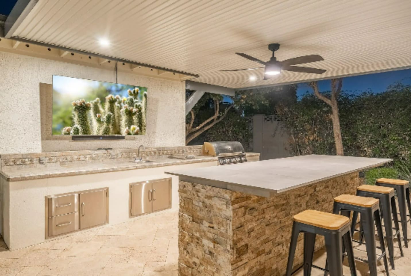 The outdoor bar seats the whole crew, with a built-in grill and big screen — this is where the party actually happens.
