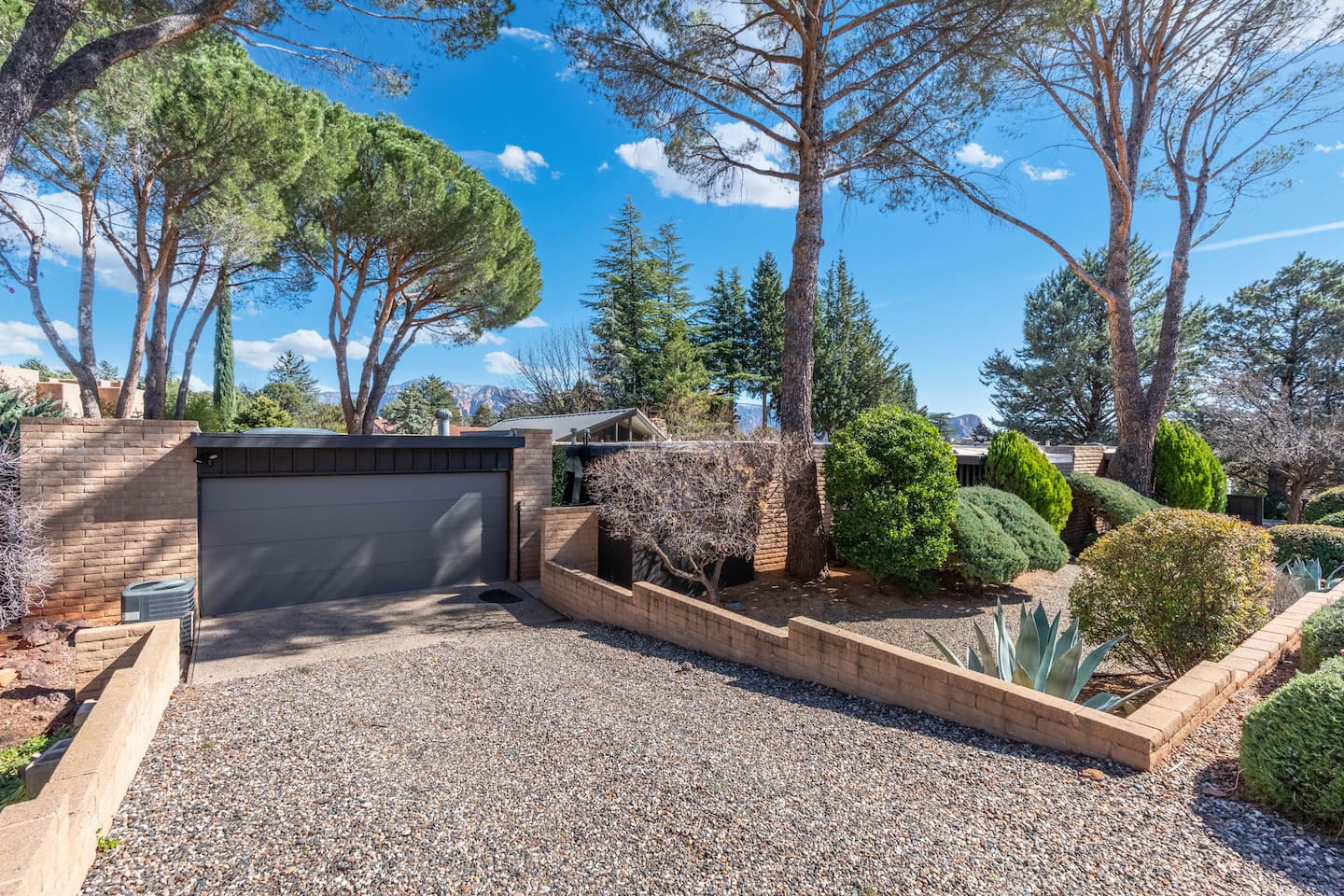 Clean, modern garage frontage with desert landscaping and mature trees creating a welcoming, private approach.