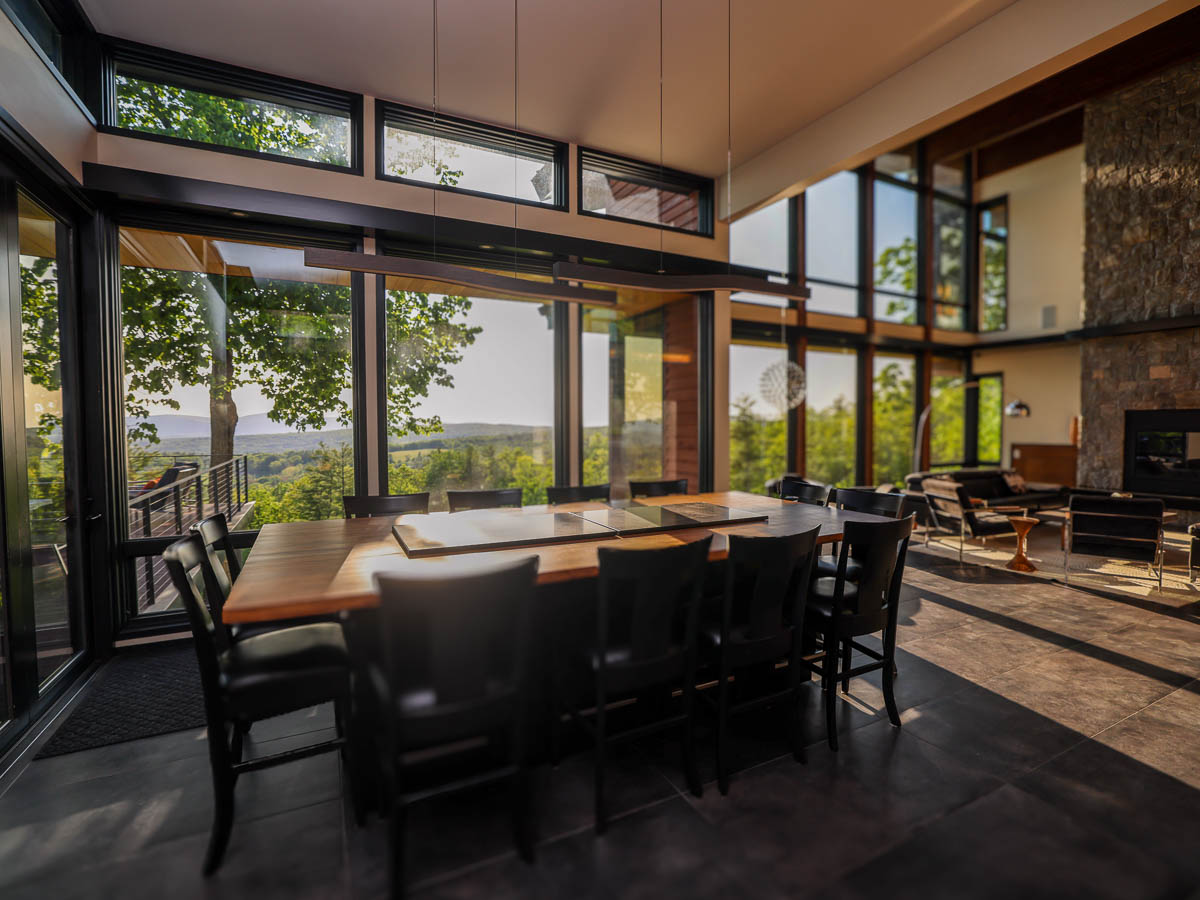 The Great Room dining table at golden hour, valley view through floor-to-ceiling glass into living &mdash; Sunset Falls Berkshires
