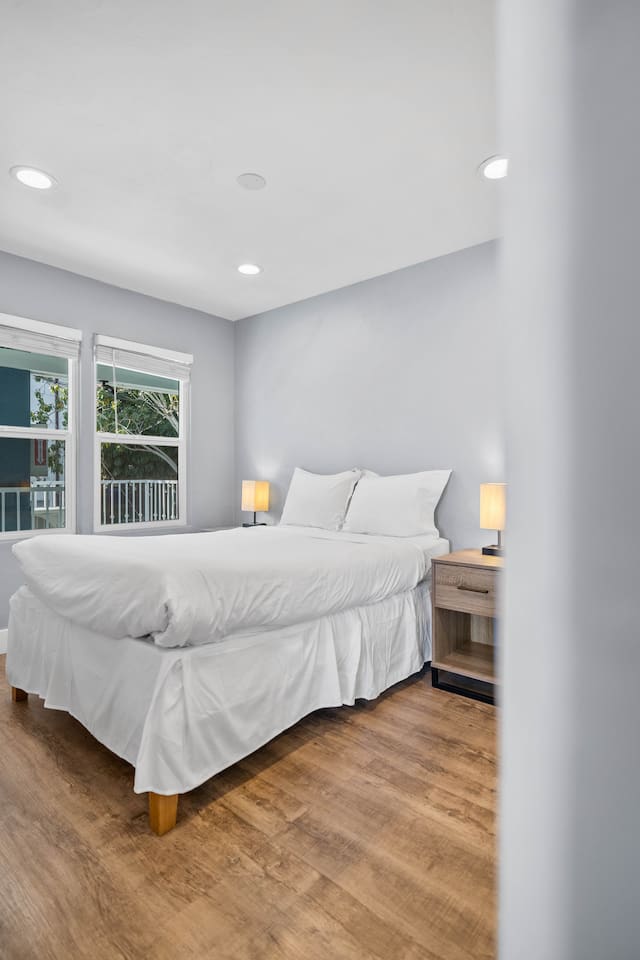 Cozy bedroom featuring a thick, comfortable bed adorned with stylish lampshades on either side. Large windows offer a beautiful morning view, filling the room with natural light and creating a serene atmosphere for relaxation and rest.