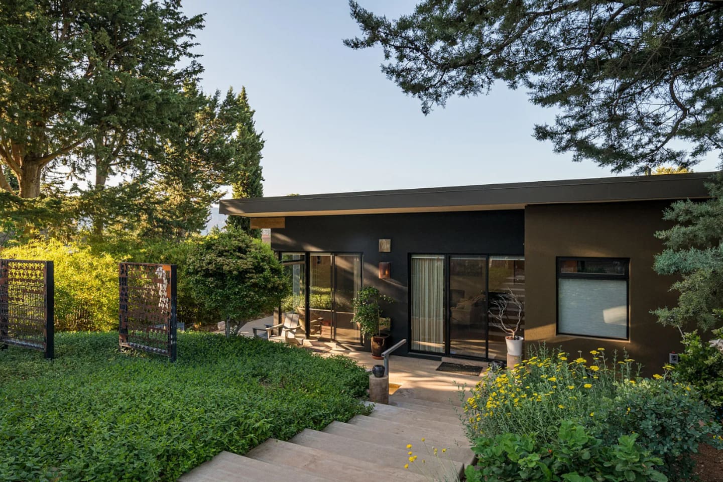 Modern exterior surrounded by vibrant greenery and blooming flowers, featuring expansive windows and a serene garden pathway.