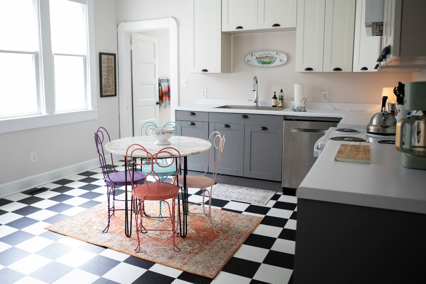 A bight, timeless full kitchen featuring classic black-and-white checkered floors, marble top bistro table for four, and generous prep space  - playful, practical and designed for real stays.