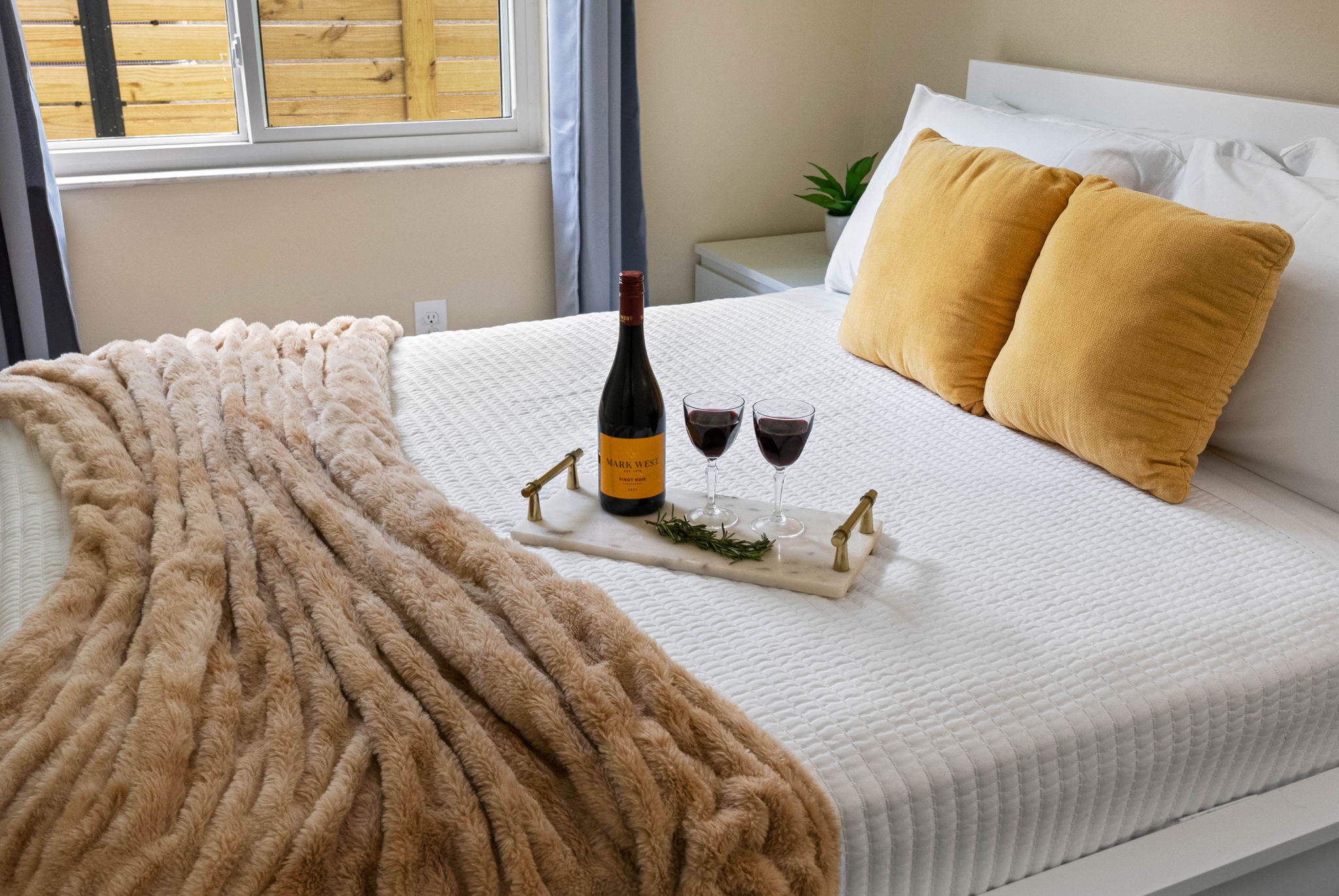 The plush bed features a white textured quilt, topped with two mustard-gold velvet accent pillows that add a pop of color and contemporary charm.