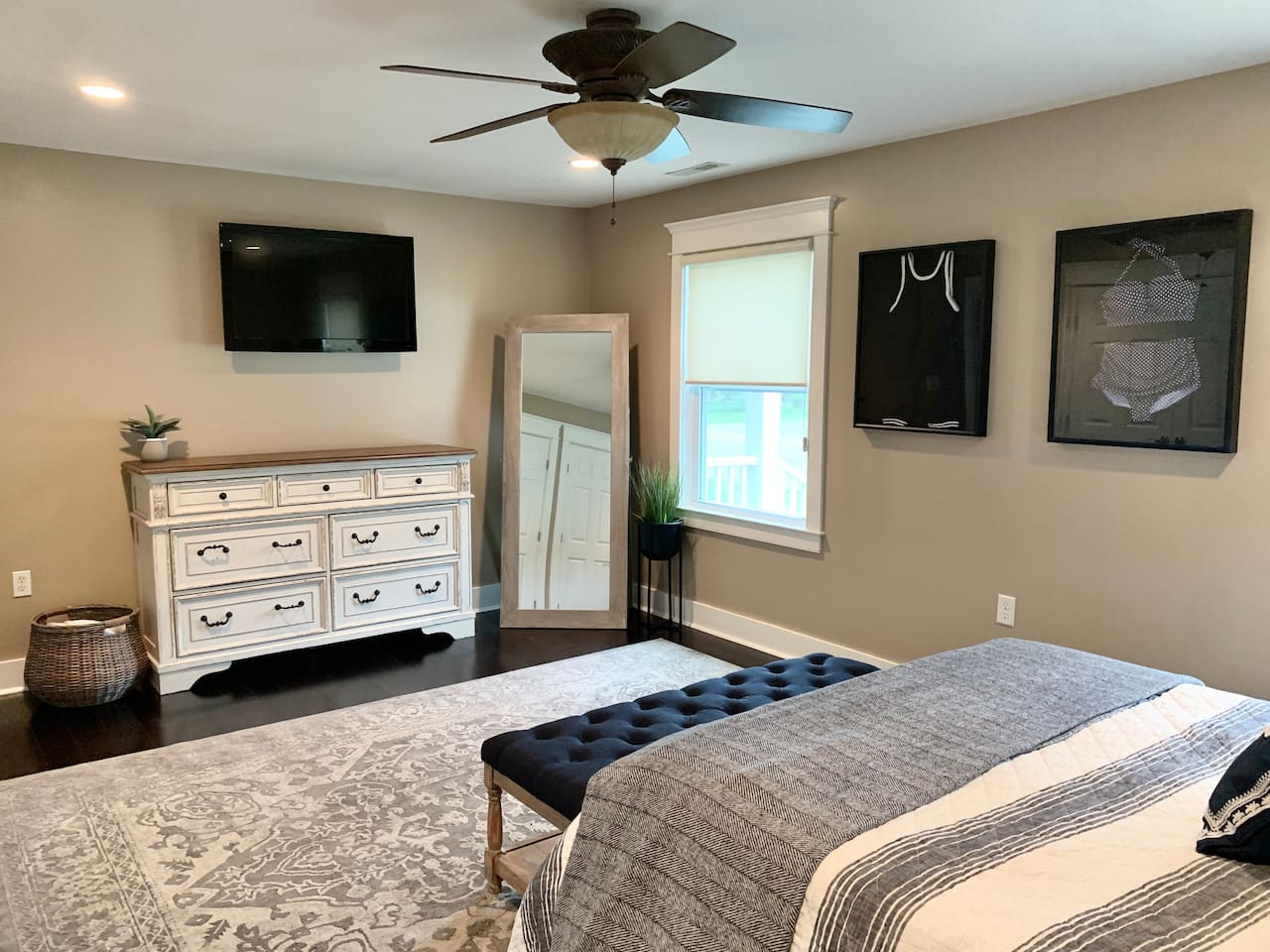 Retreat to this stylish bedroom featuring a large dresser, wall-mounted TV, and full-length mirror. Coastal-themed artwork and a plush tufted bench add a sophisticated touch, making it the perfect place to recharge after a day at the beach.