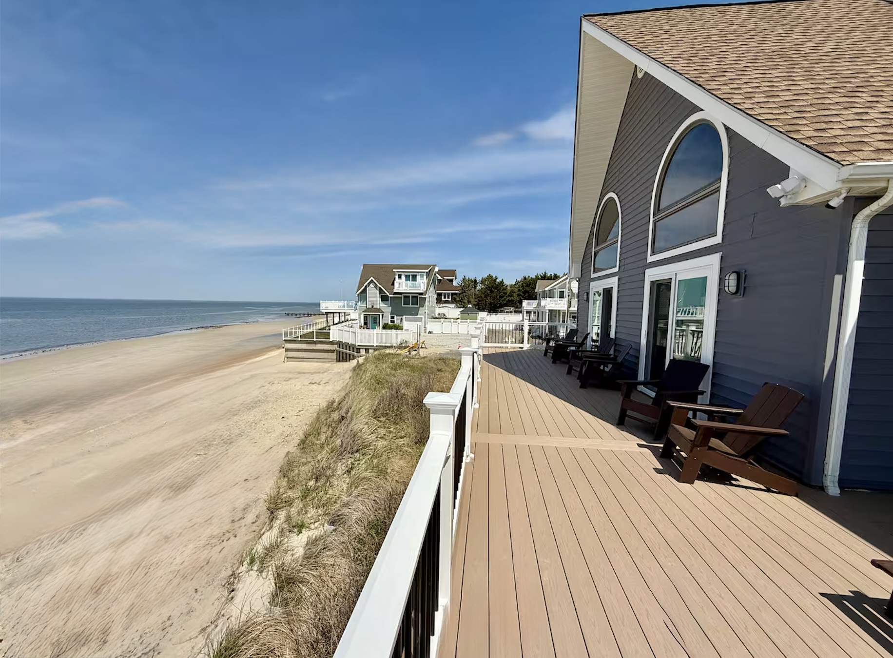 You can enjoy a scenic beachfront view from the property's spacious, elevated deck. This outdoor area is perfectly furnished with lounge chairs, offering an ideal space to relax and experience the coastal environment.