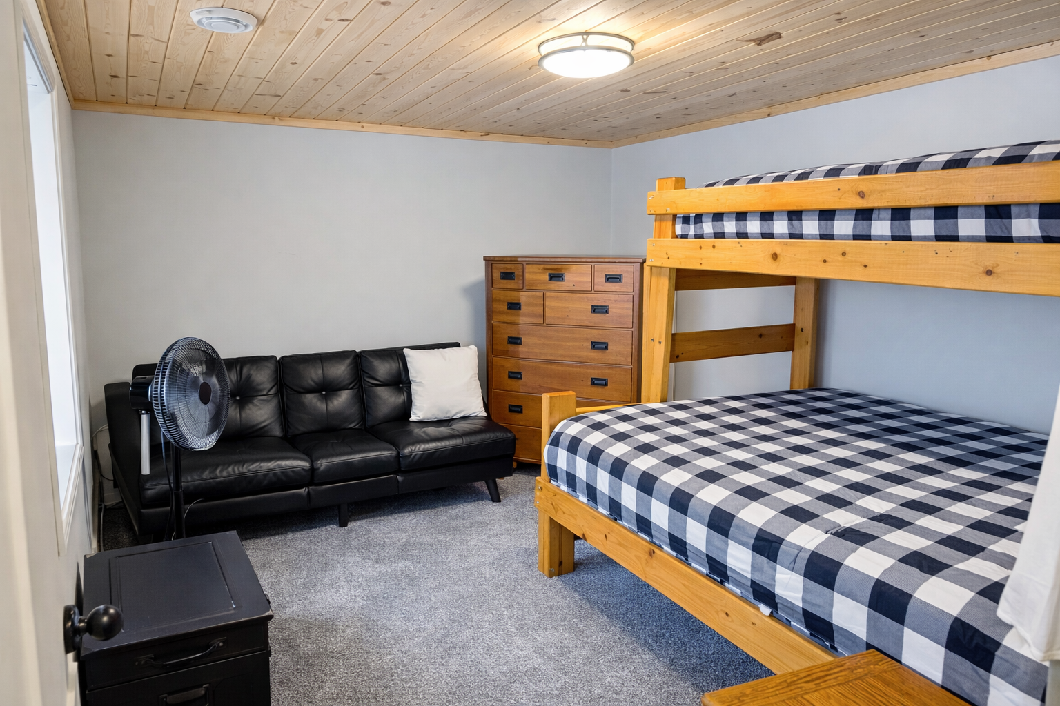 This downstairs bedroom features a full-over-queen bunk bed, a futon couch for lounging, a large dresser for storage, and a fan to keep things cool. It’s a comfy, practical space to relax after a day out, perfect for family or friends.
