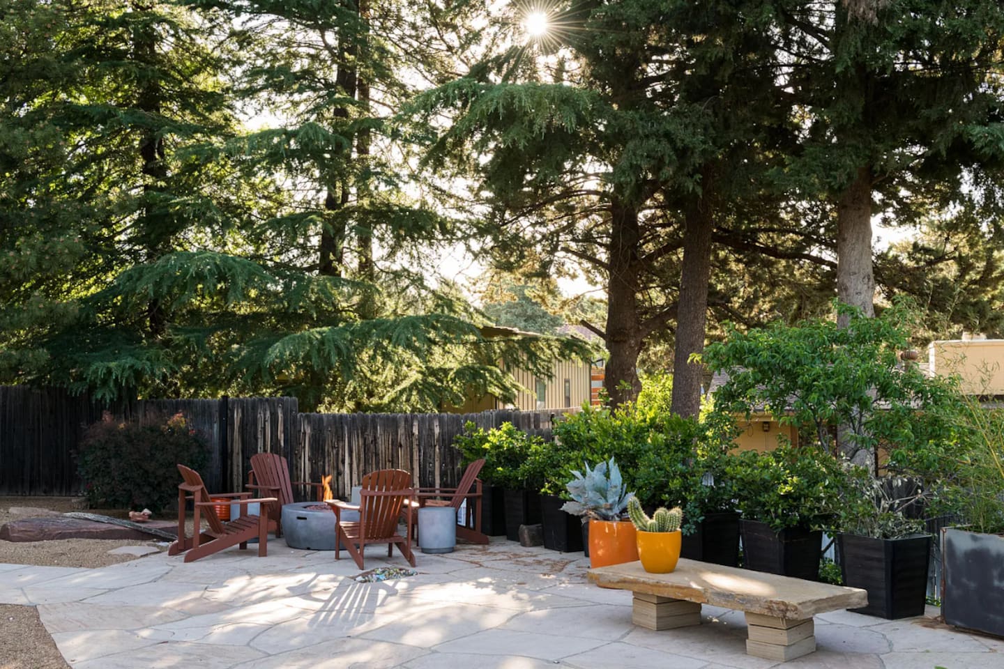 Peaceful backyard patio surrounded by mature trees and lush greenery, featuring comfortable seating and a fire pit — an ideal space to relax and enjoy the outdoors.