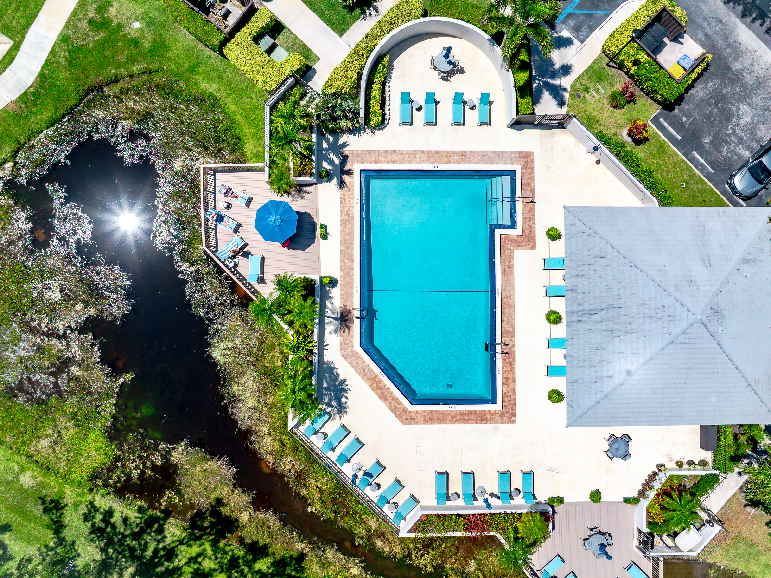 Resort-style heated community pool surrounded by lush tropical landscaping, sun loungers, and peaceful lake views — perfect for relaxing after a day at the beach or golf course.

