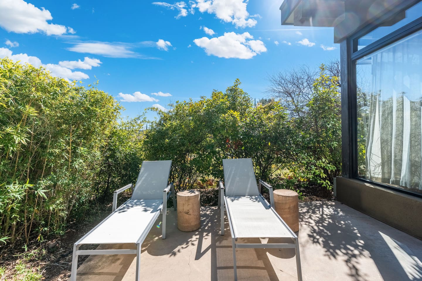 Sunny private patio with two lounge chairs and lush greenery for peaceful outdoor relaxation.