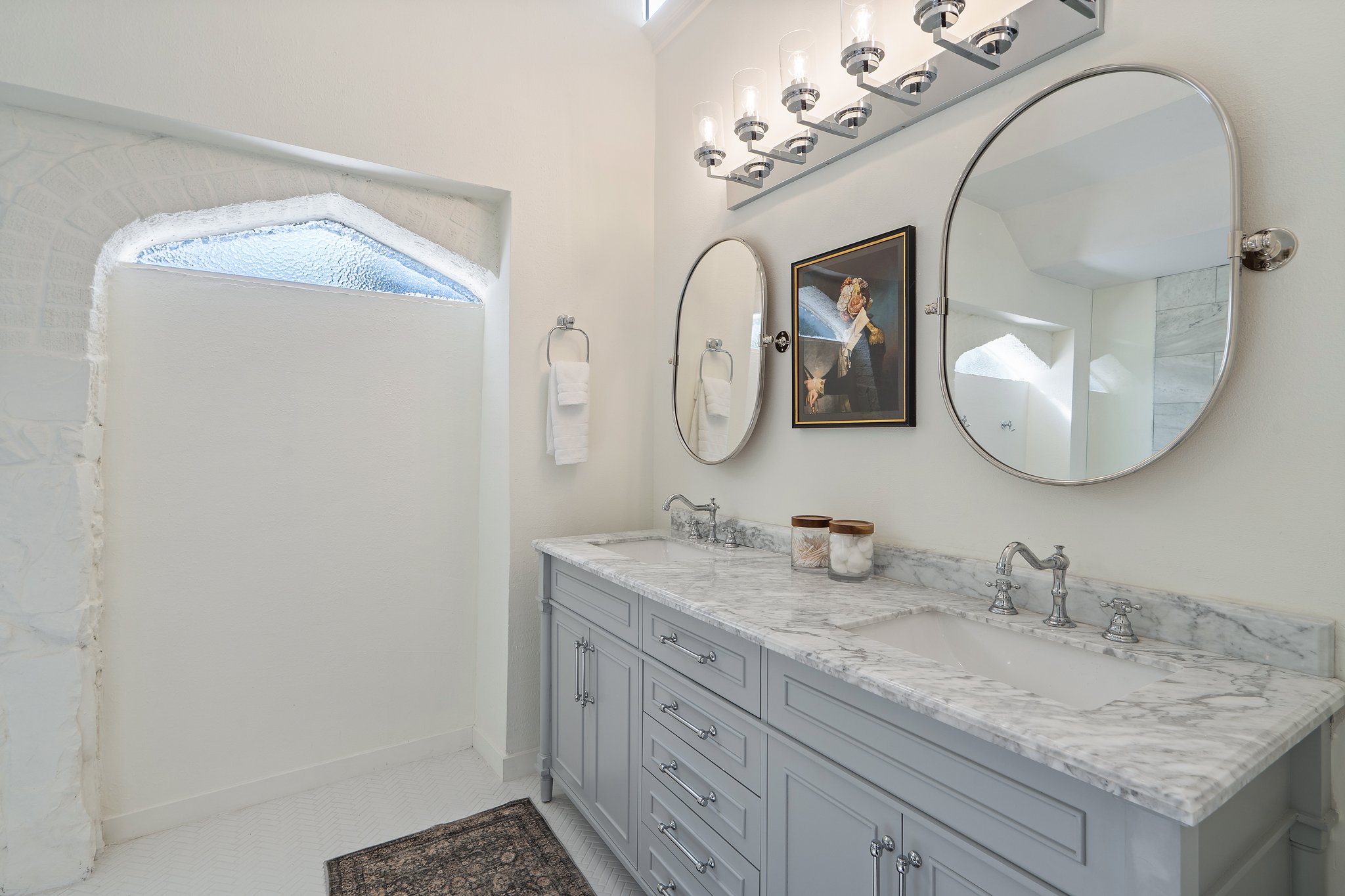 Bathroom 1 dual-sink vanity with round mirrors and updated matte fixtures. Fresh towels, hairdryer, and Ginger Lily Farms shampoo, conditioner, and shower gel provided. Main house, first floor.