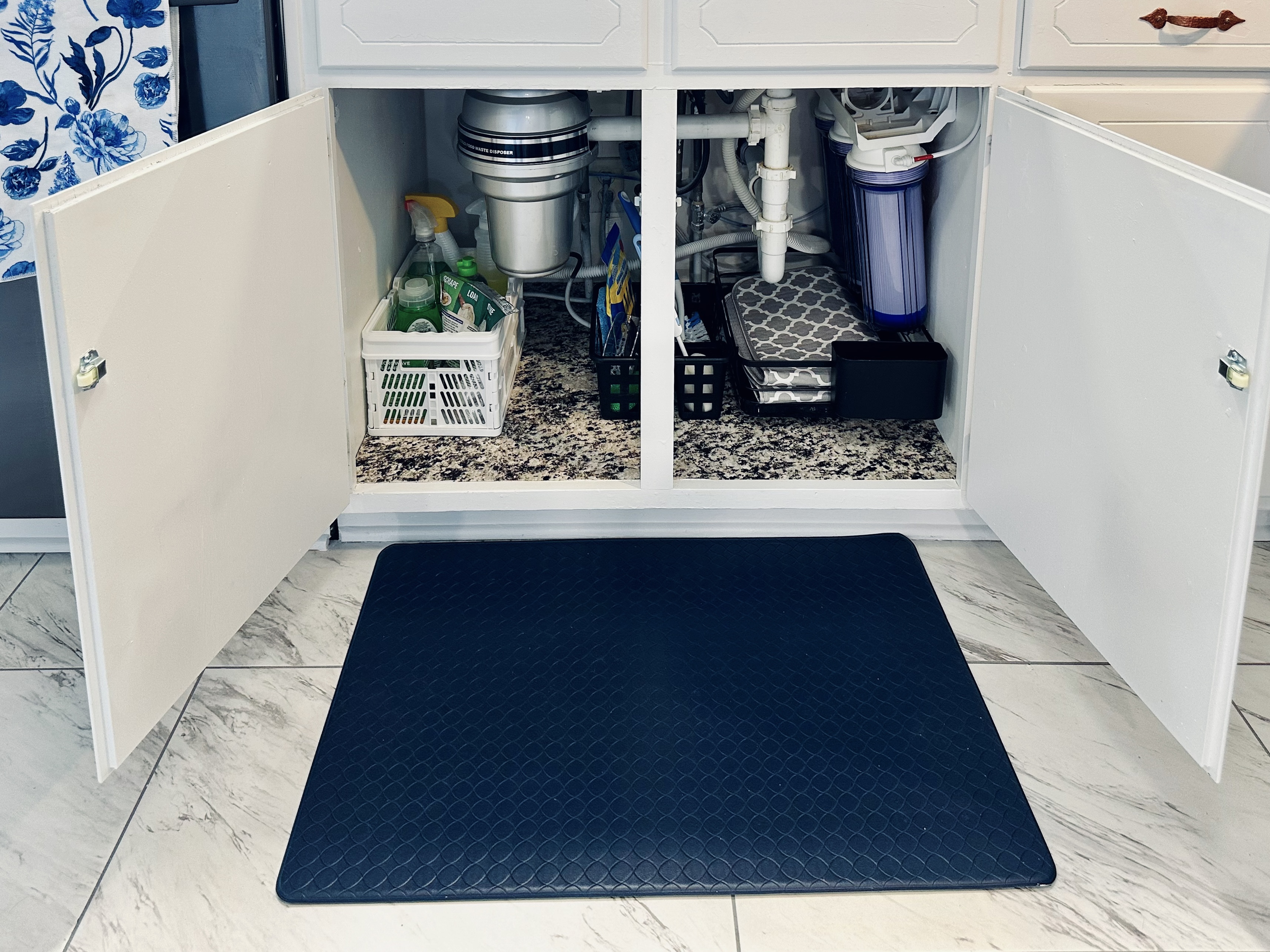Under-sink cabinet stocked with kitchen cleaning essentials, including dishwasher detergent, dish soap, sponge, gloves, bottle scrubber, dish drying rack and mat, and additional cleaning supplies.