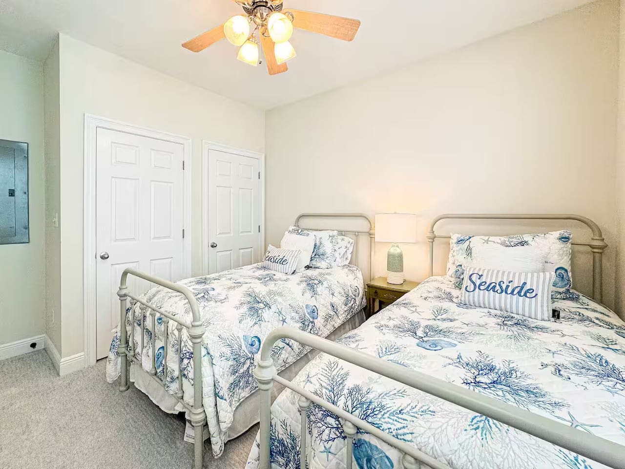 Bright guest bedroom with two twin beds, coastal-themed linens, and plenty of natural light. Includes a ceiling fan and cozy setup—perfect for kids or friends.