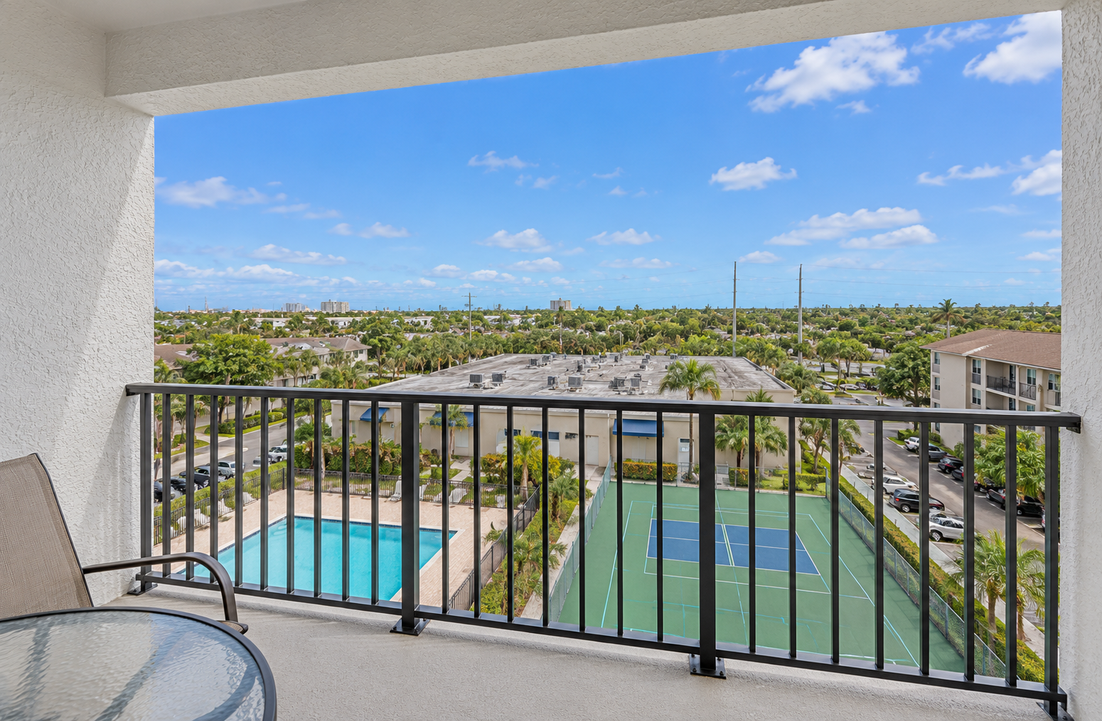 Covered balcony with table seating, chairs, and a treetop view over the Holiday Towers area.